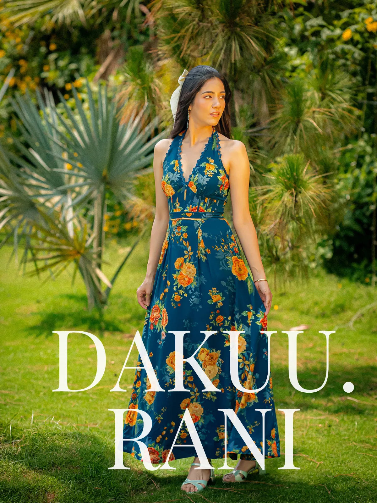 Woman wearing the Pretty Pixie Dakuu Rani floral halter-neck maxi dress, posing in a lush garden setting for a summer fashion editorial.