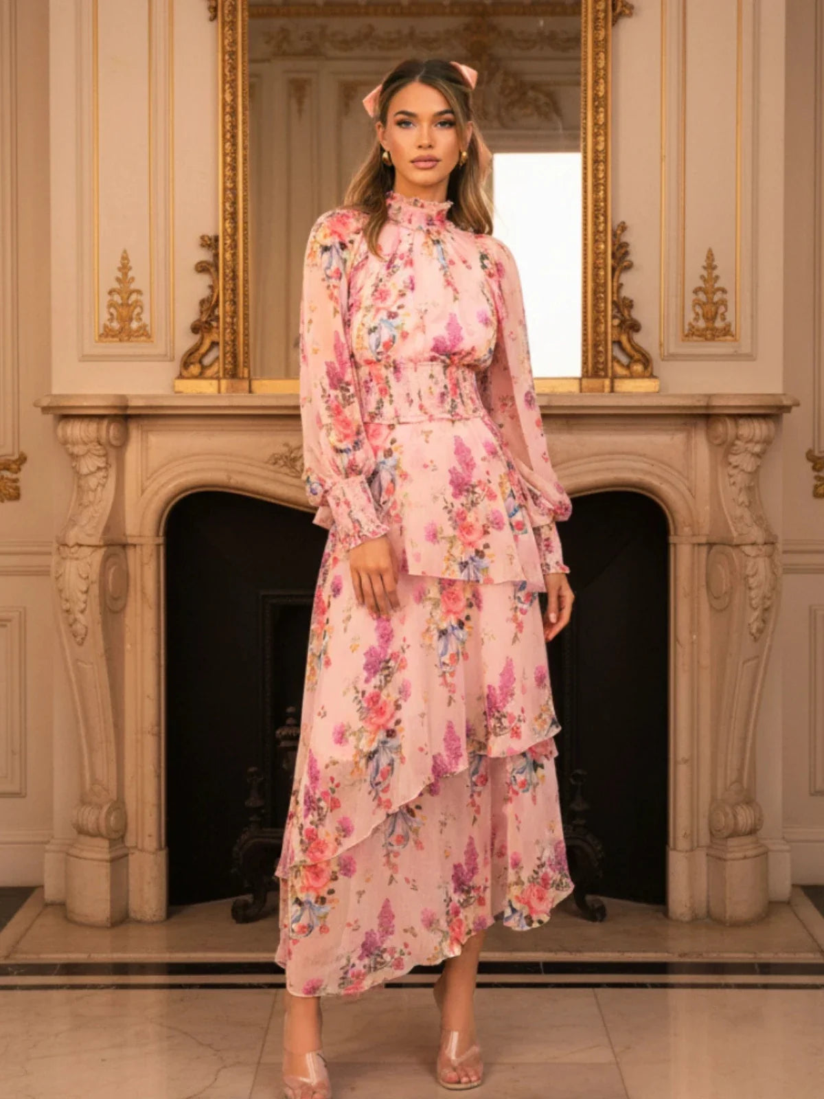 Woman wearing a Pretty Pixie pink floral layered maxi dress with full sleeves, styled in an elegant indoor setting for a luxury fashion editorial.