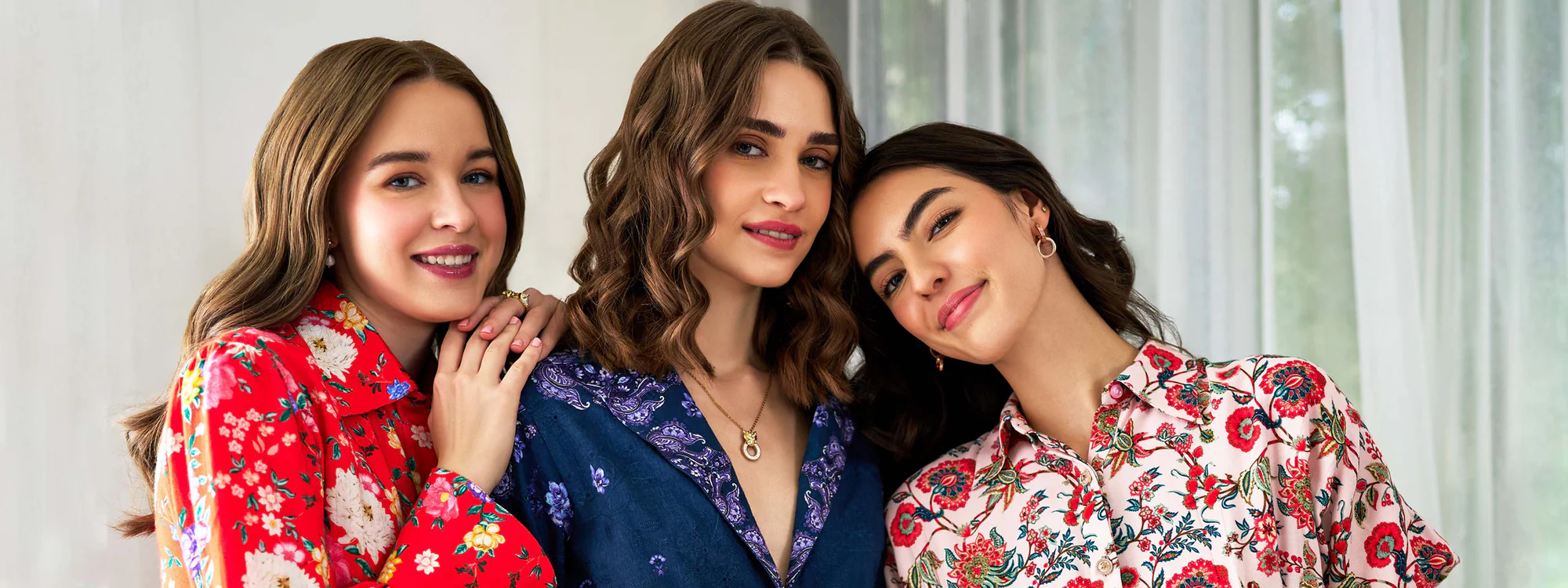Three women smiling in vibrant floral print dresses, showcasing Pretty Pixie's modern spring fashion collection indoors