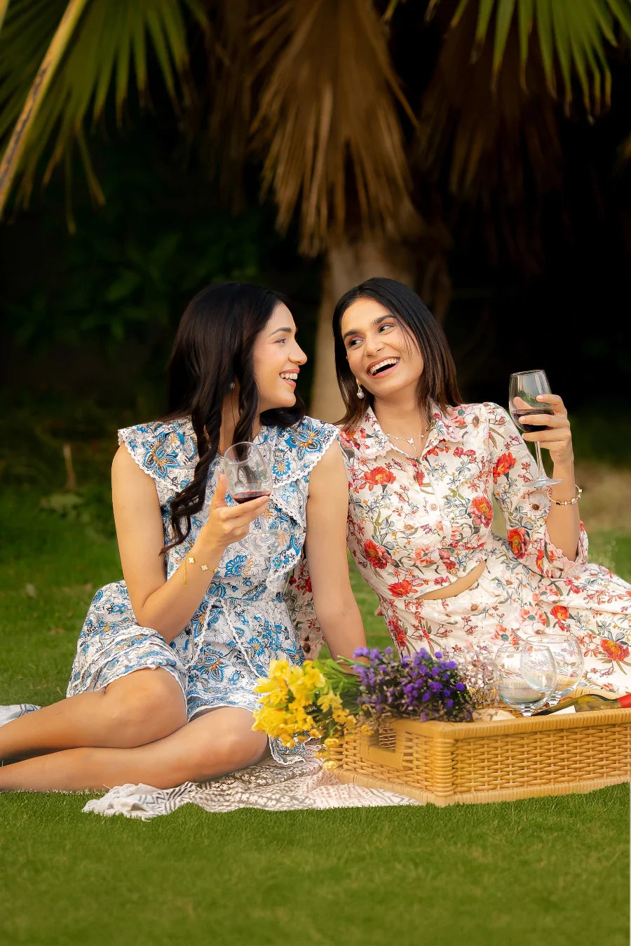Two women enjoying a picnic in a park, holding glasses of wine.