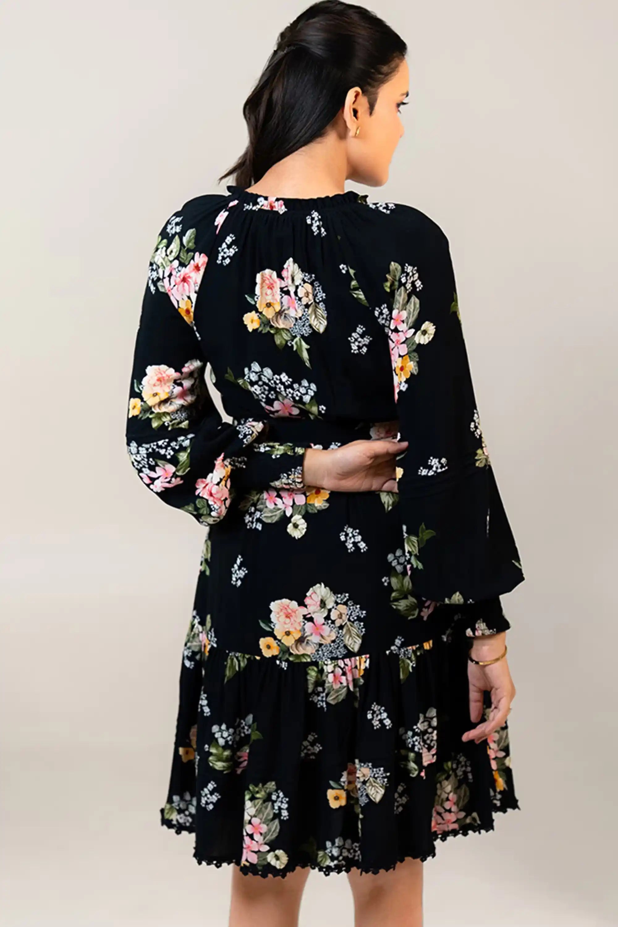 Back view of black floral belted mini dress with fitted waistline.