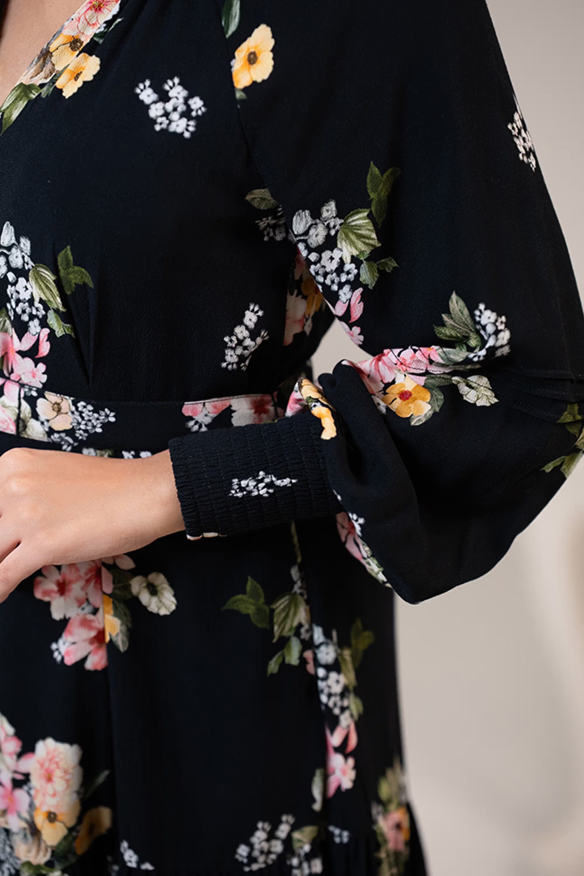 Closeup of sleeve cuff and floral prints on black belted short dress with long sleeves