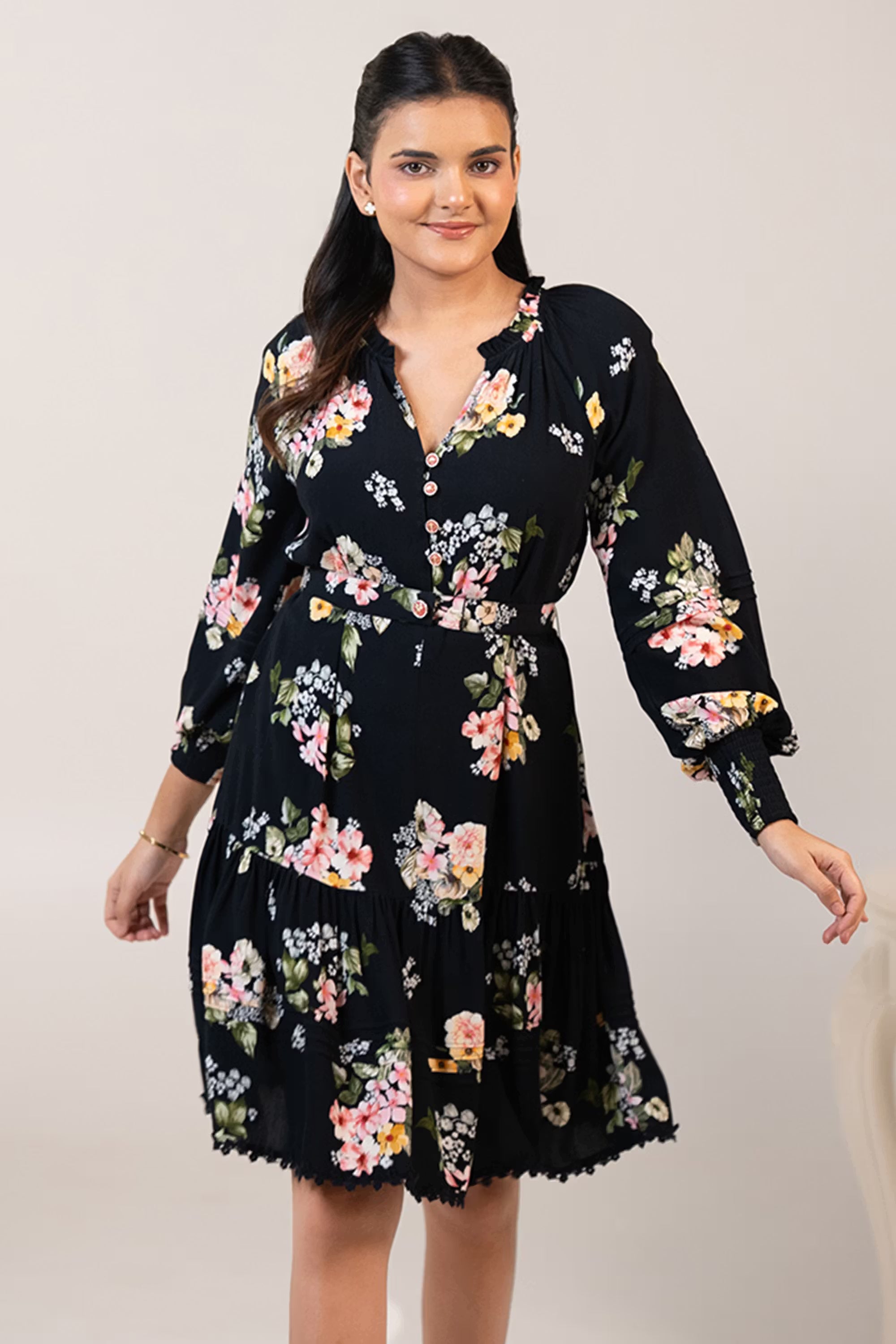 Model smiling in black floral short dress with waist tie and button-front neckline