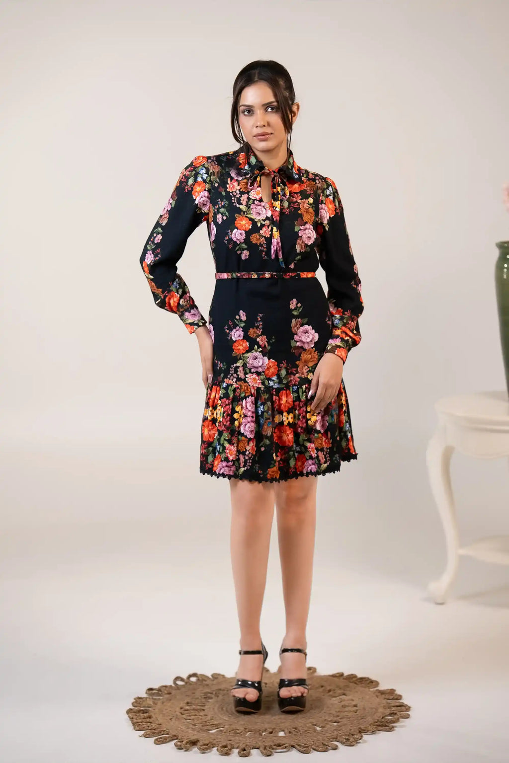 Back view of black floral dress with bow-tie neckline, long sleeves, and pleated ruffle hem