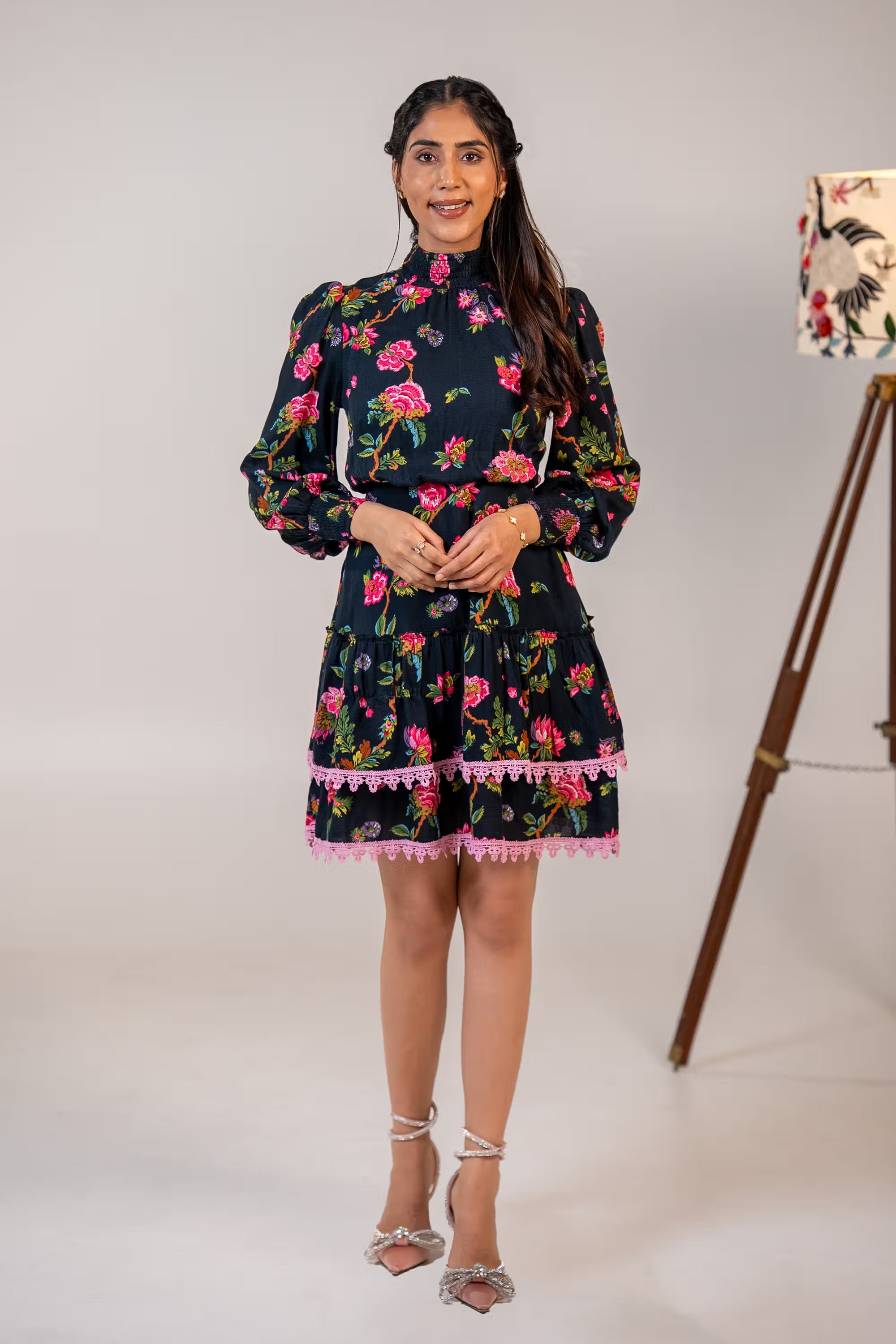 Front view of black floral mini dress with pink lace trim, long puff sleeves, and high neckline.