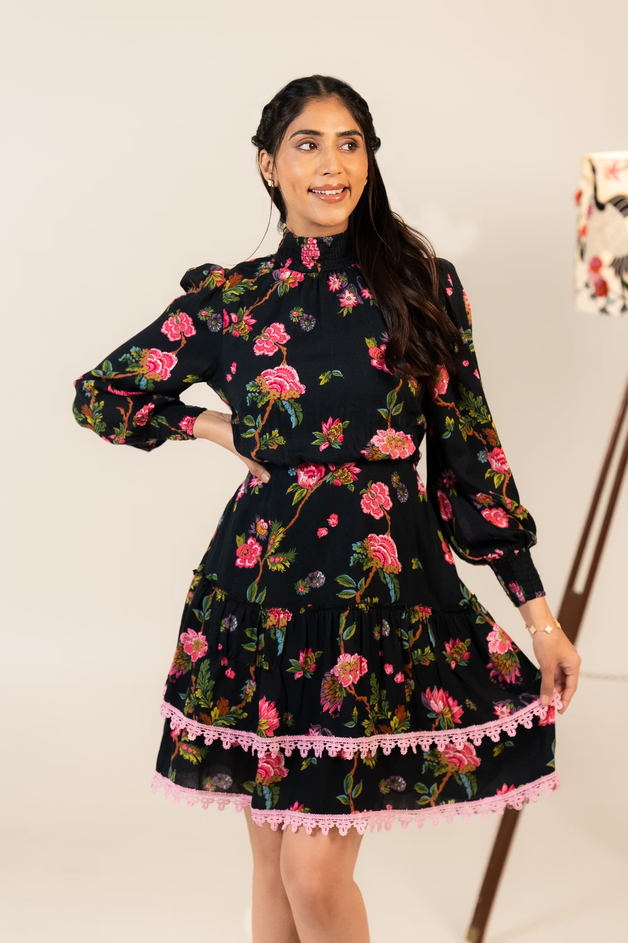Side pose of black floral mini dress featuring pink lace trim, floral print, and elegant long sleeves.