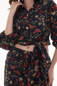 Woman in Pretty Pixie black floral tie-front crop top & co-ord set, close-up of knotted waist and puff sleeves