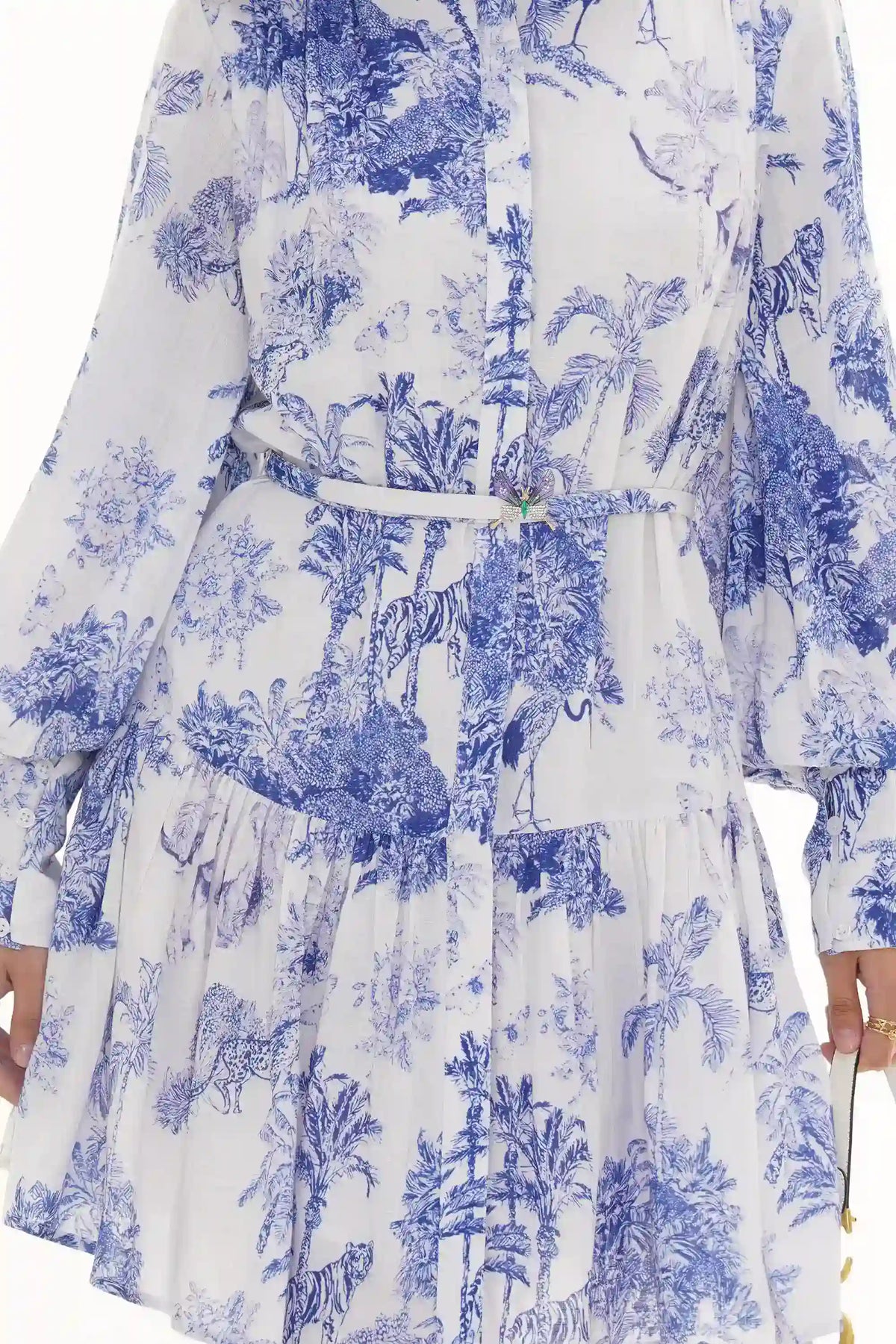 Woman in Pretty Pixie blue and white toile jungle-print belted tiered dress with butterfly brooch