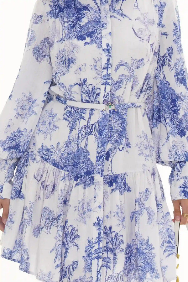 Woman in Pretty Pixie blue and white toile jungle-print belted tiered dress with butterfly brooch