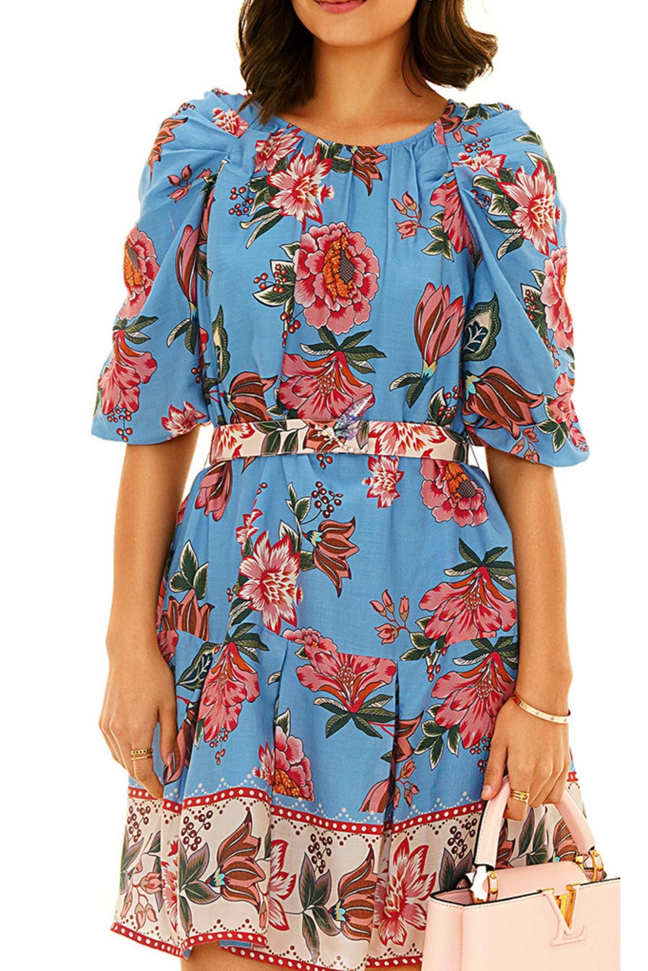 A woman elegantly poses in a blue floral dress adorned with delicate pink flowers, exuding grace and style.
