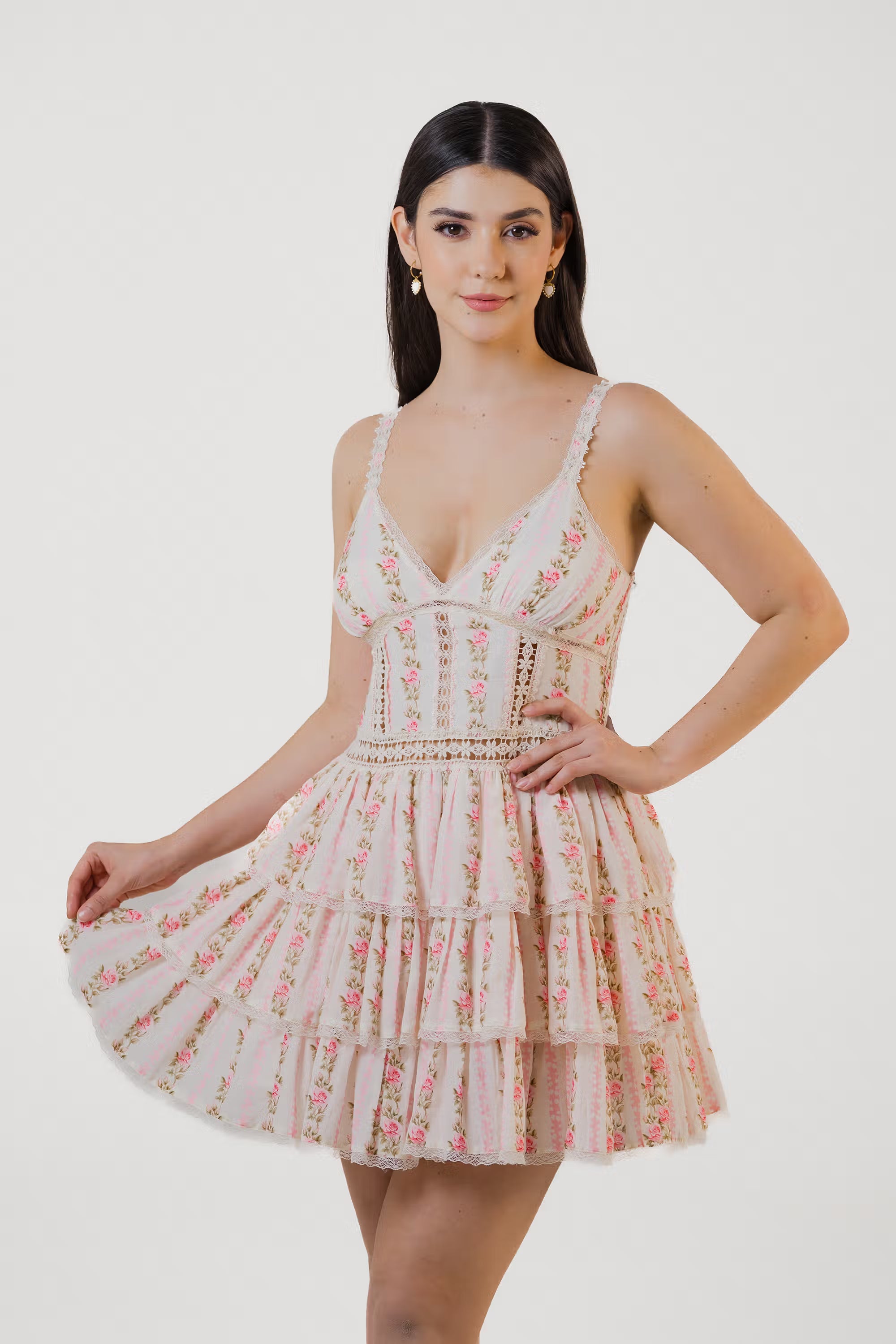 Model holding hem of pink floral ruffle mini dress with lace trim and layered tiers