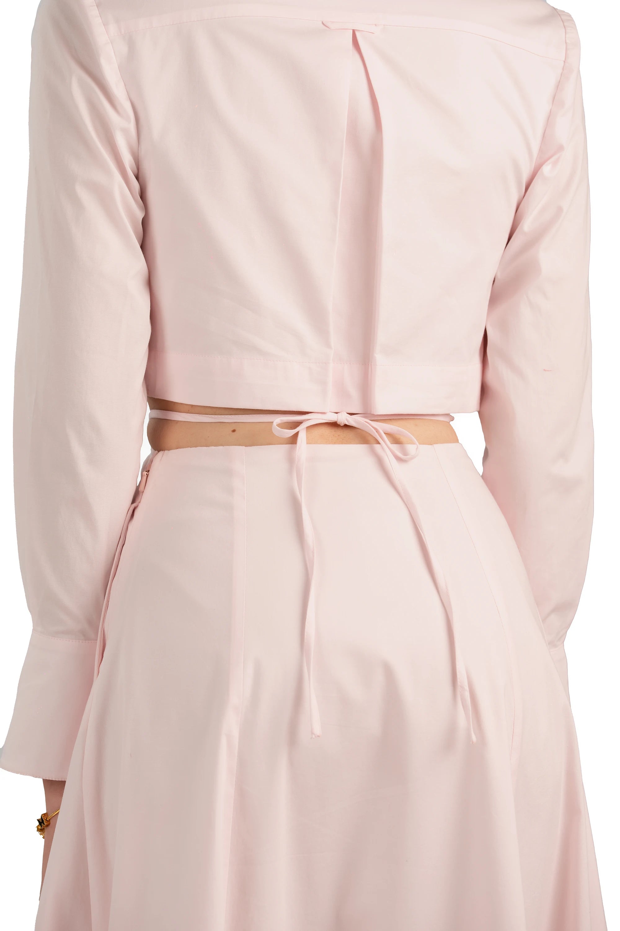 Back view of blush pink maxi dress with long sleeves, tie-back detail, and waist cutout design.