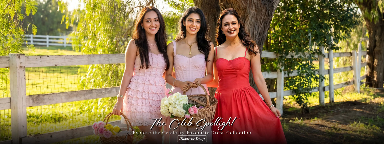 Three women in pink red and cream dresses by fence holding flowers baskets celebrity collection