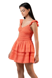Side view of coral smocked mini dress with ruffle sleeves and tiered hemline