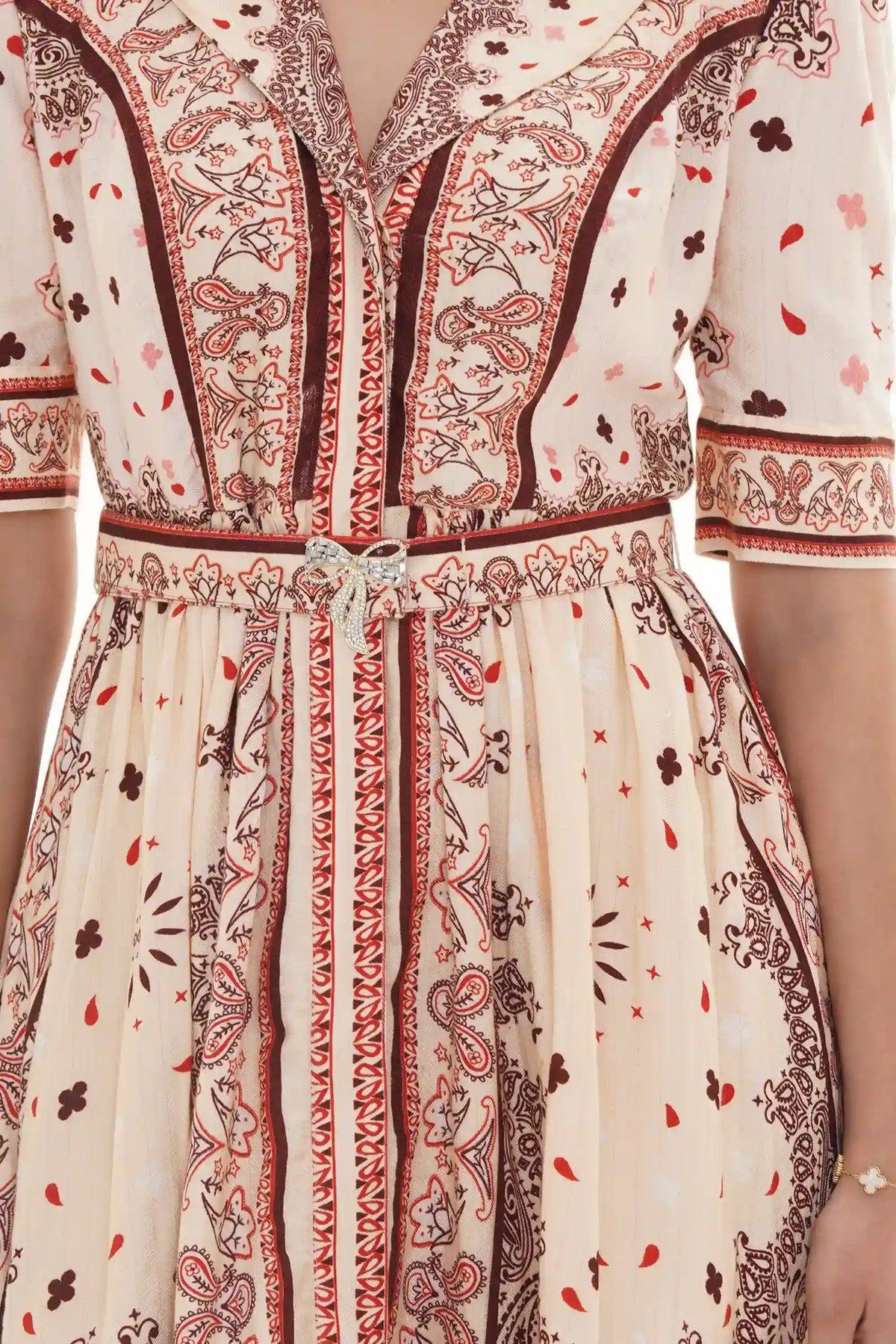 Close-up of Pretty Pixie cream bandana-print collared belted dress with crystal bow brooch waist detail