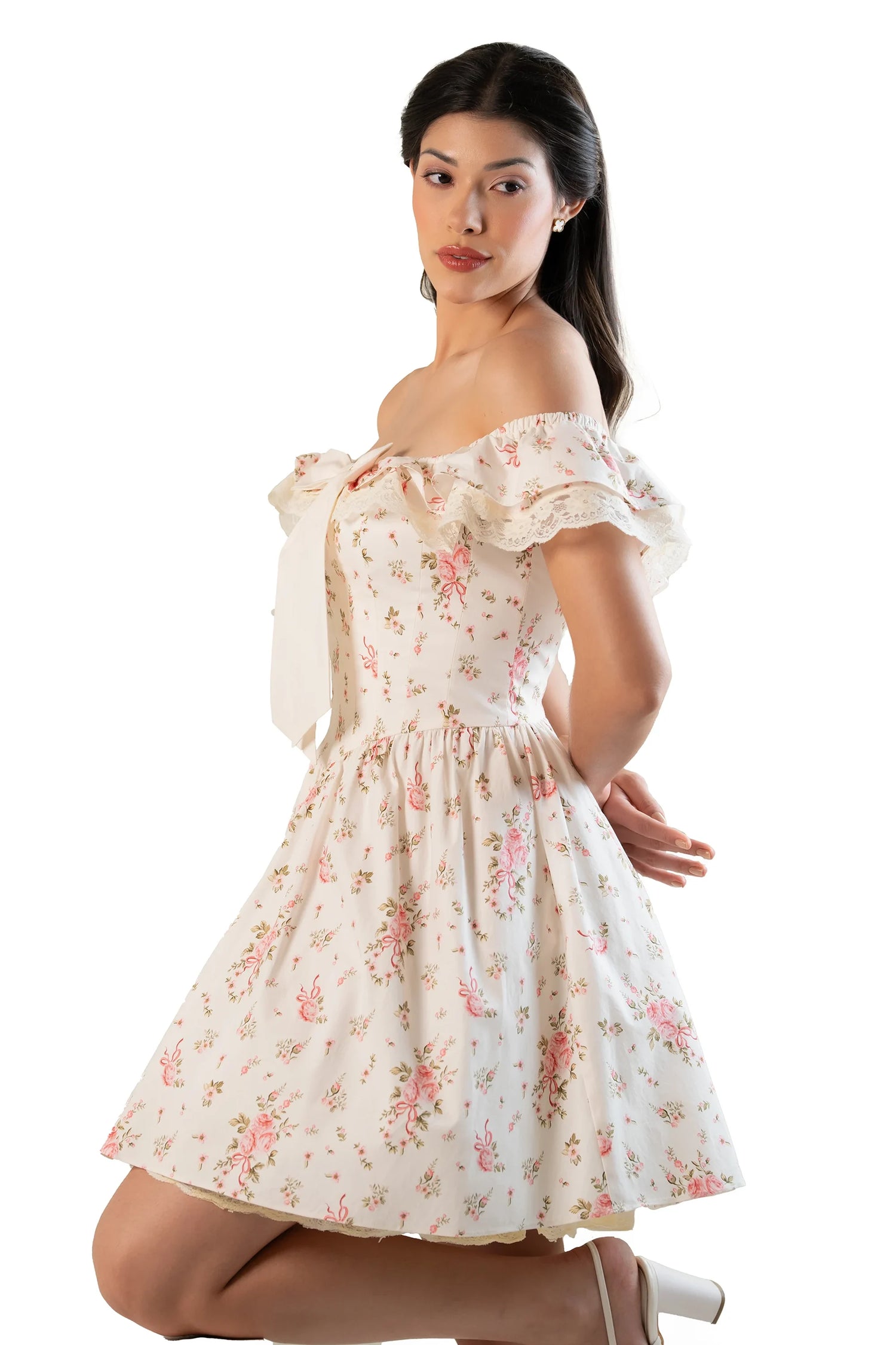 Model kneels in cream floral off-shoulder mini dress with ruffled sleeves and flared skirt.