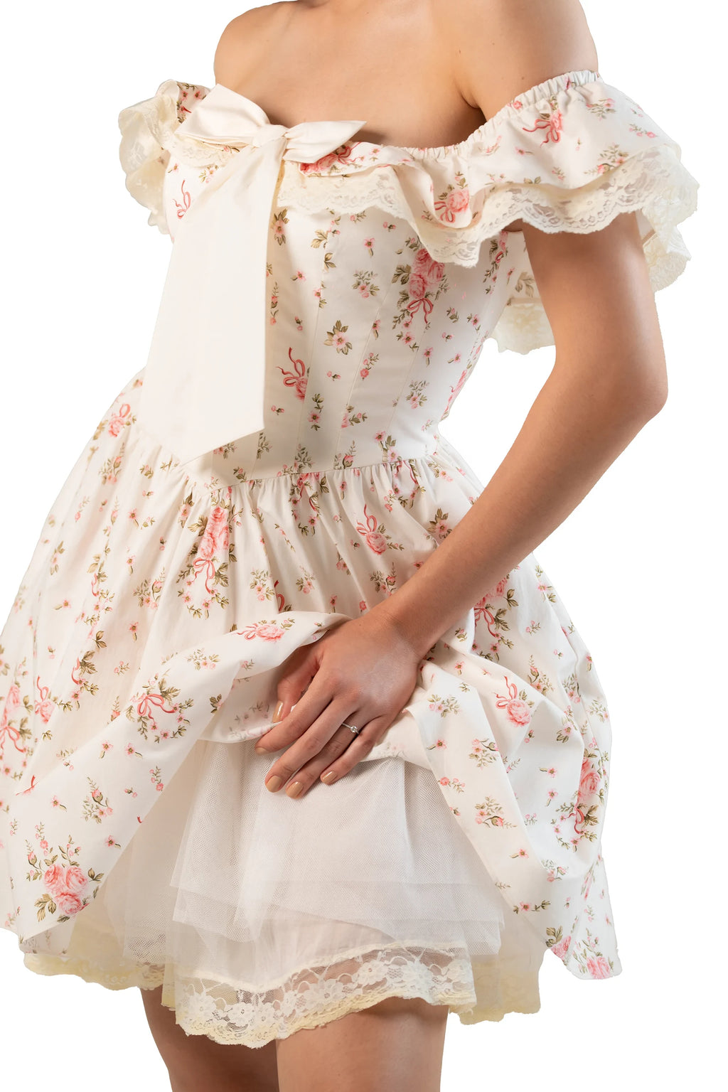 Close-up of cream off-shoulder mini dress showing bow, ruffled neckline, and tulle underskirt.