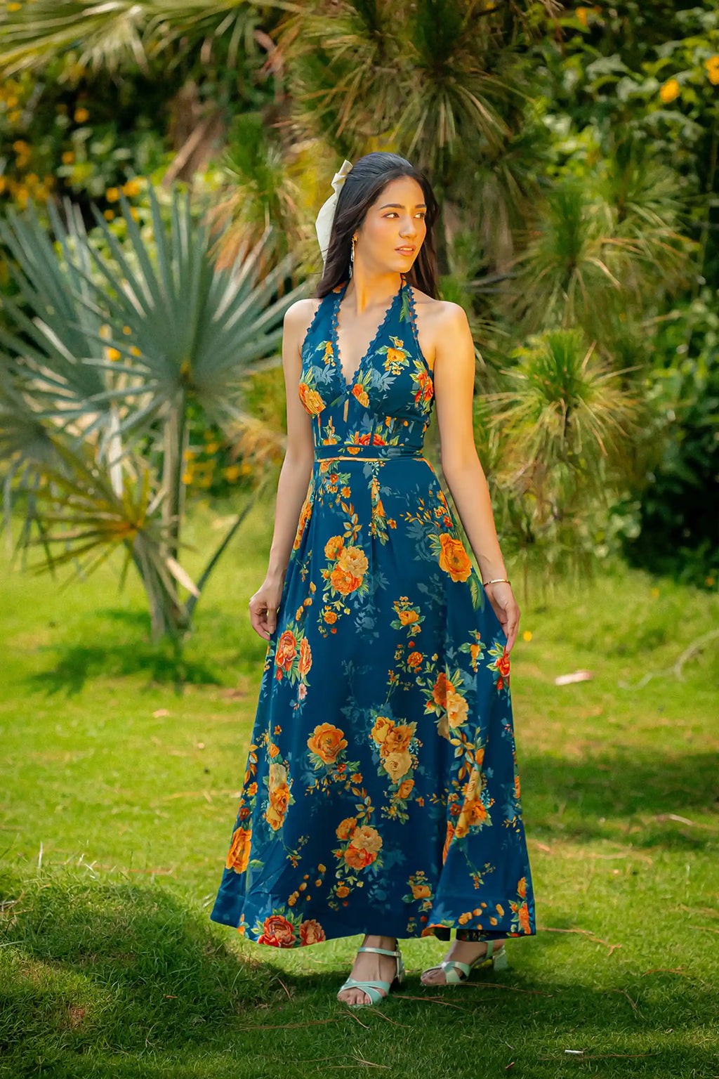 Front view of dark teal halter neck floral maxi dress with garden backdrop