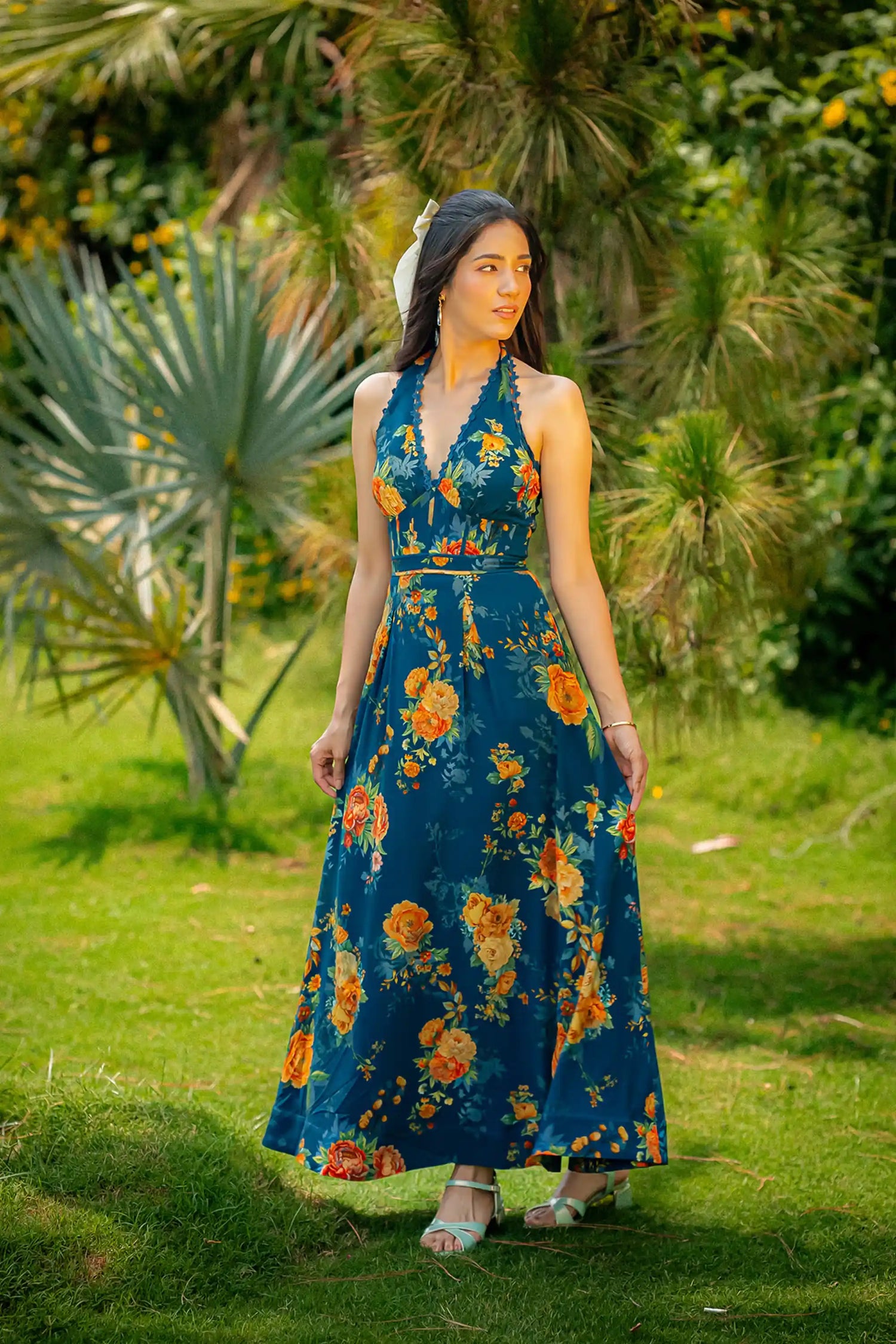 Front view of dark teal halter neck floral maxi dress with garden backdrop