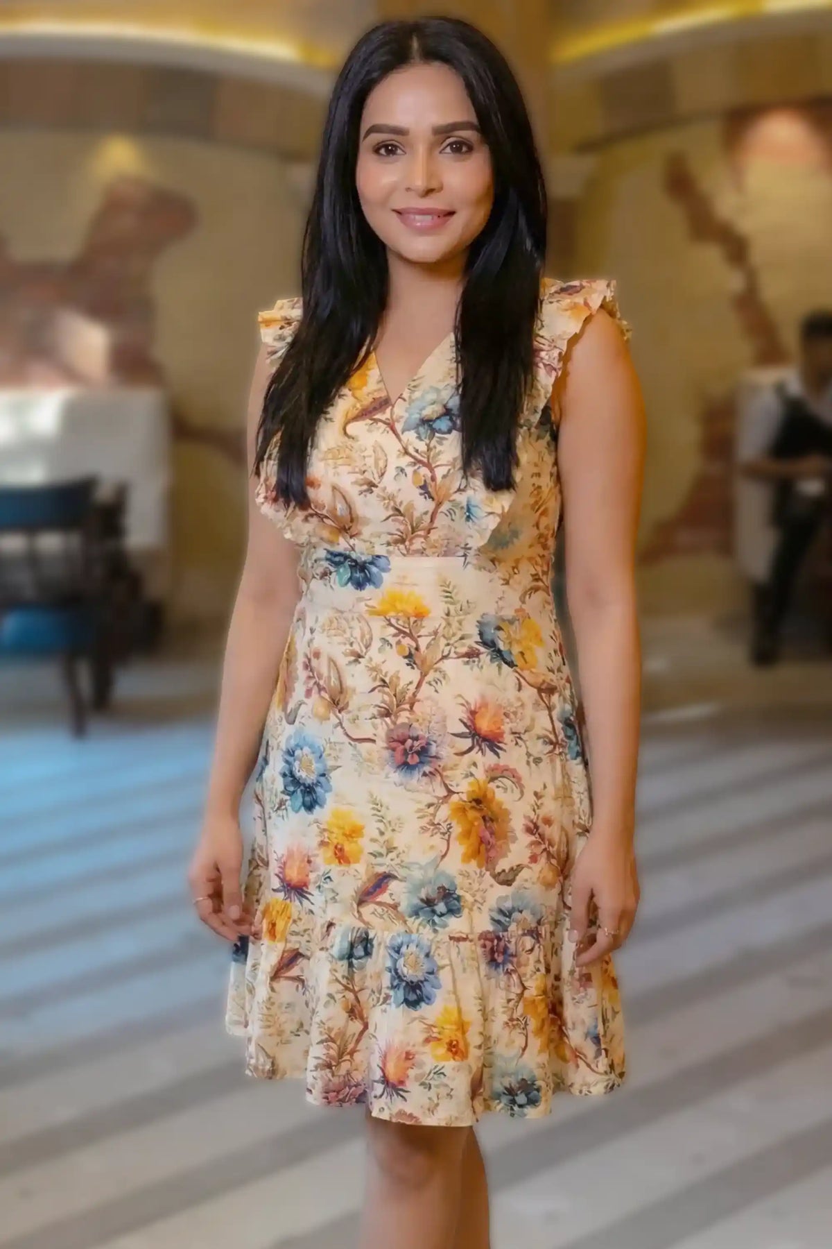 Woman wearing a floral midi dress standing indoors in an elegant lobby setting, styled for a fashion photoshoot.