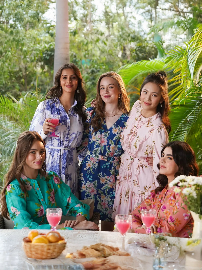 Five women in colorful floral midi dresses enjoying a garden brunch around a table with drinks and snacks, daytime get-together India.