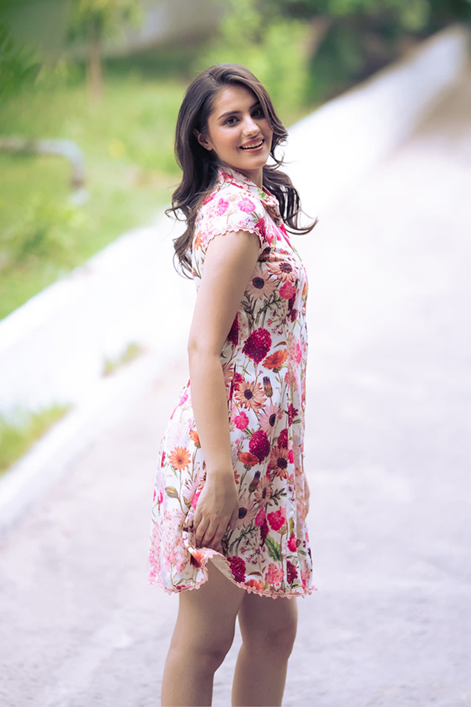 Playful outdoor pose in ivory floral sleeveless shirt dress with collared neckline and lace hem