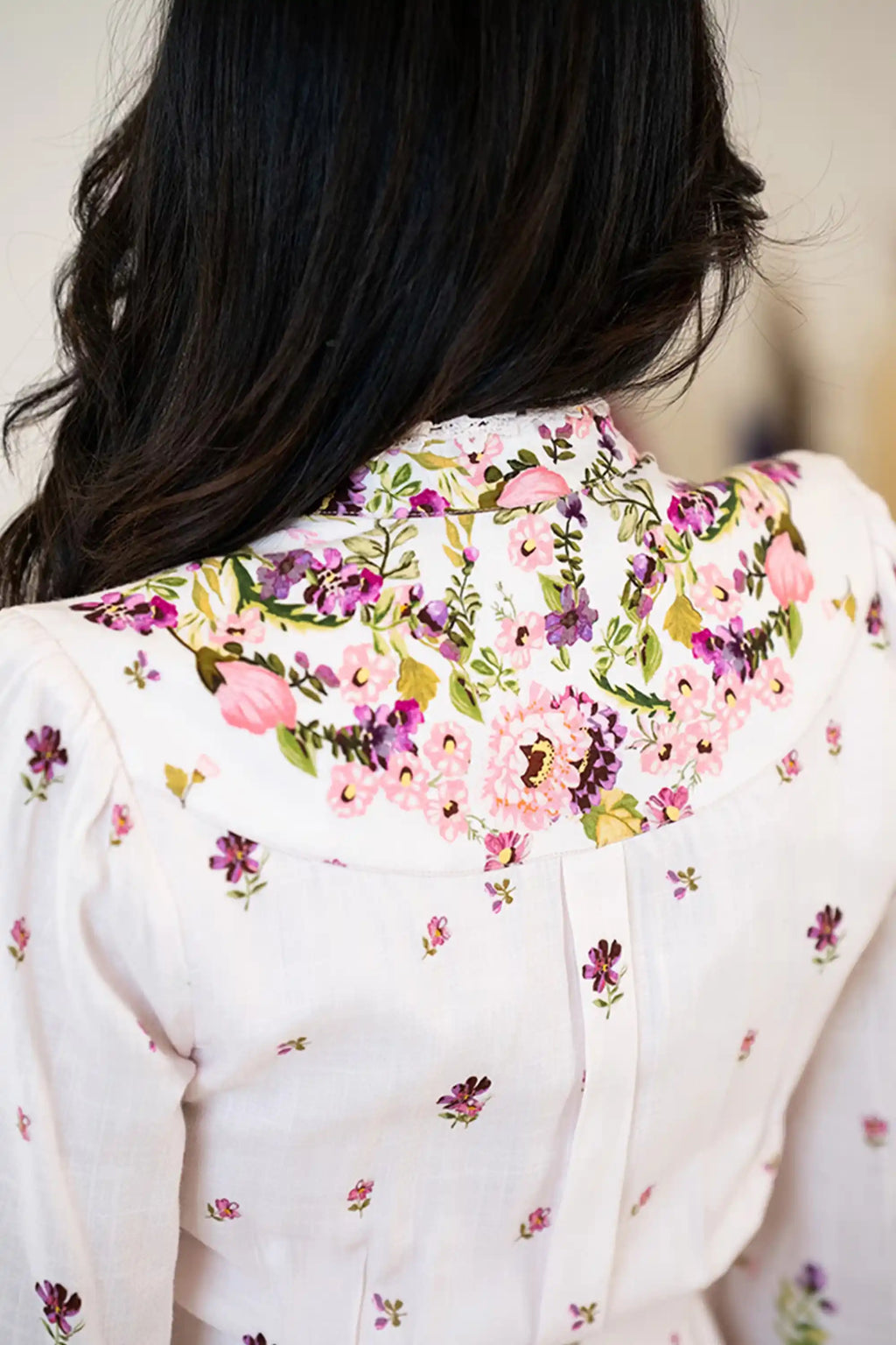 Close-up of the back neckline of a white floral dress with intricate pink and purple flower print and lace trim.