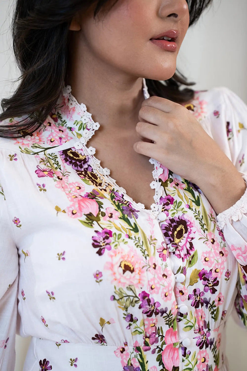 Close-up of floral printed white dress showing lace-trimmed neckline, fabric-covered buttons, and vibrant pink and purple flower design.