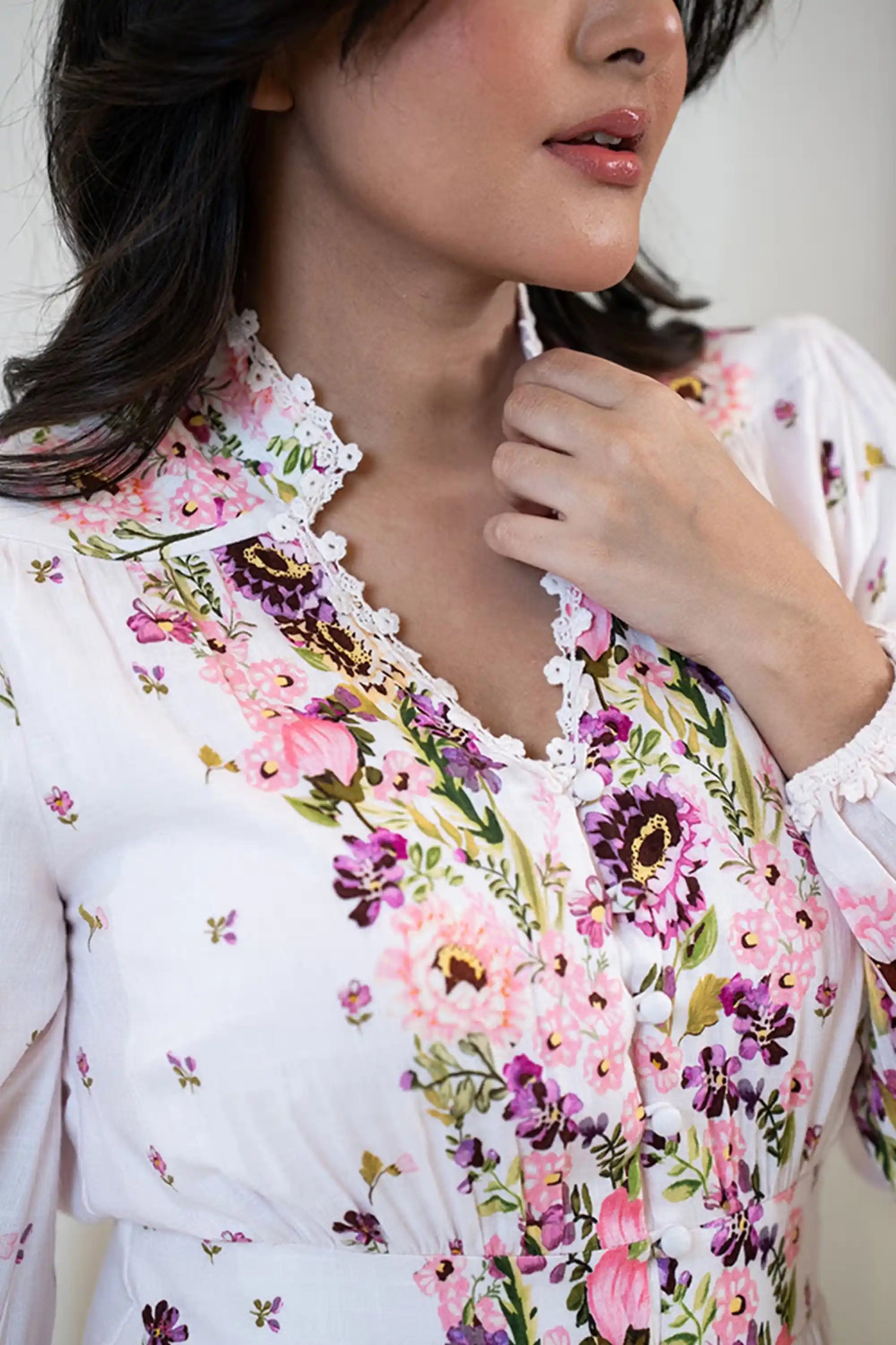 Close-up of floral printed white dress showing lace-trimmed neckline, fabric-covered buttons, and vibrant pink and purple flower design.