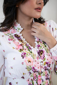 Close-up of floral printed white dress showing lace-trimmed neckline, fabric-covered buttons, and vibrant pink and purple flower design.