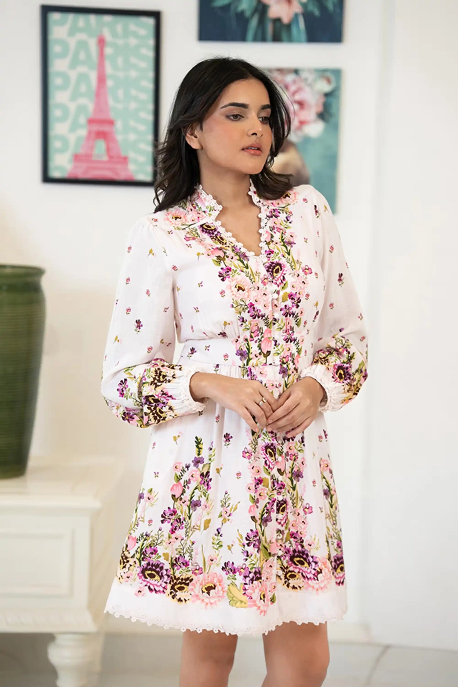 Front view of woman wearing a white mini dress with pink and purple floral prints, lace-trimmed neckline, and long sleeves