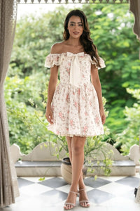 Woman in ivory floral lace trim off-shoulder mini dress with ruffle neckline pink roses garden