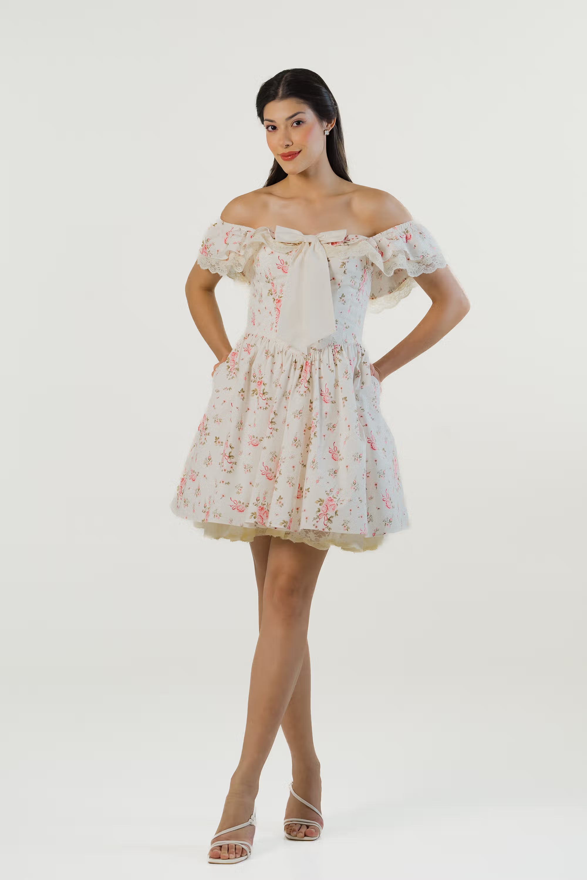 Woman wearing ivory off-shoulder floral mini dress with bow detail and lace trim, front view.