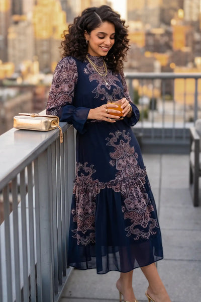 Woman smiling on a city rooftop in the evening wearing Pretty Pixie's Kaitlyn navy paisley long-sleeve midi dress