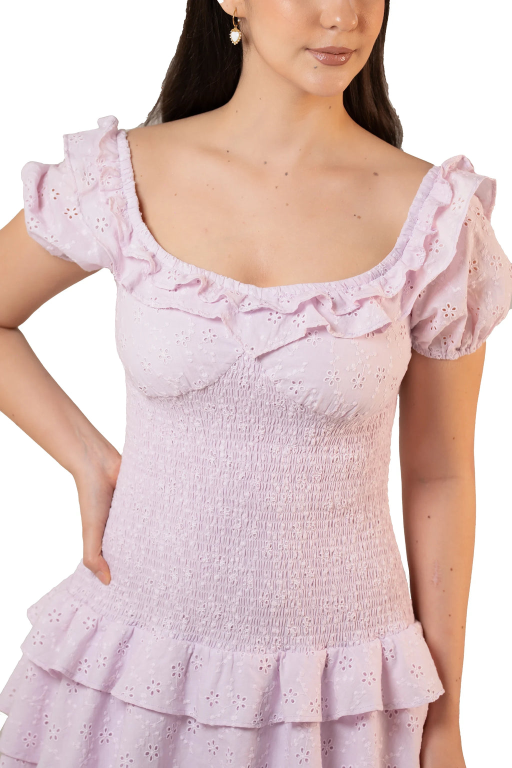 Close-up of smocked bodice on lavender eyelet dress with ruffled scoop neckline, puff sleeves, and floral cutwork details.