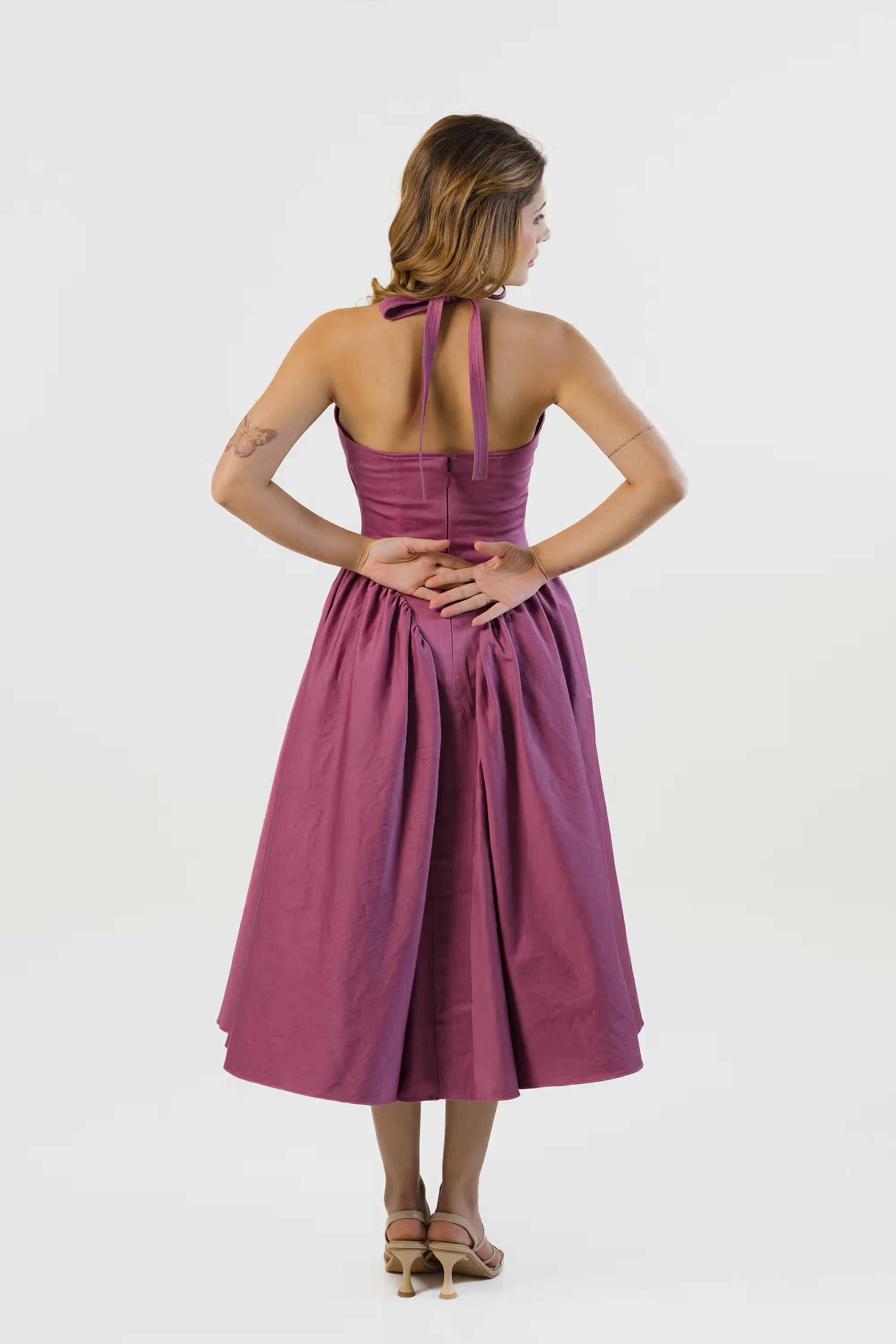 Back view of plum halter midi dress with halter tie straps and fitted waistline.