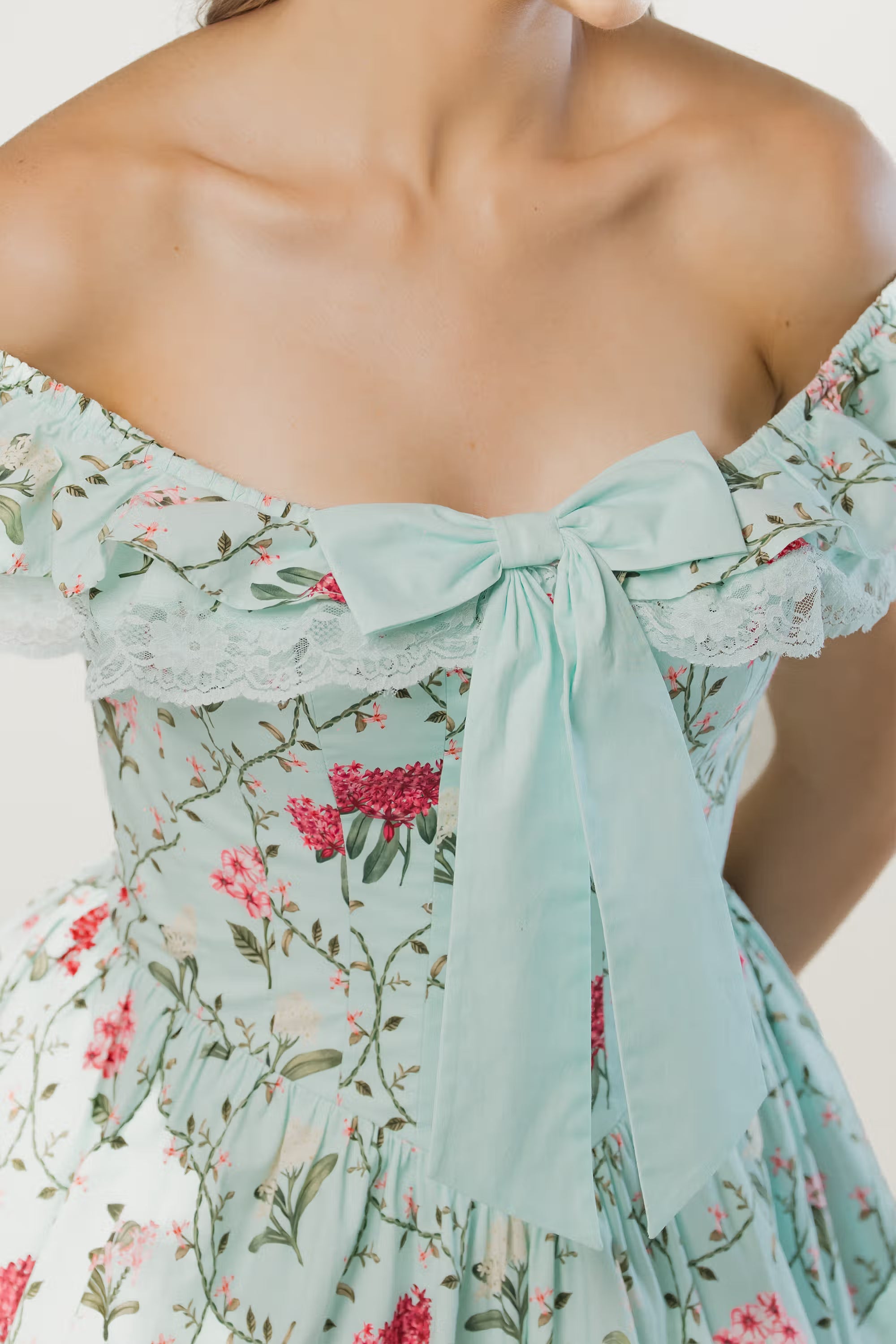 Close-up of mint green off-shoulder floral dress with oversized bow tie and lace trim detail