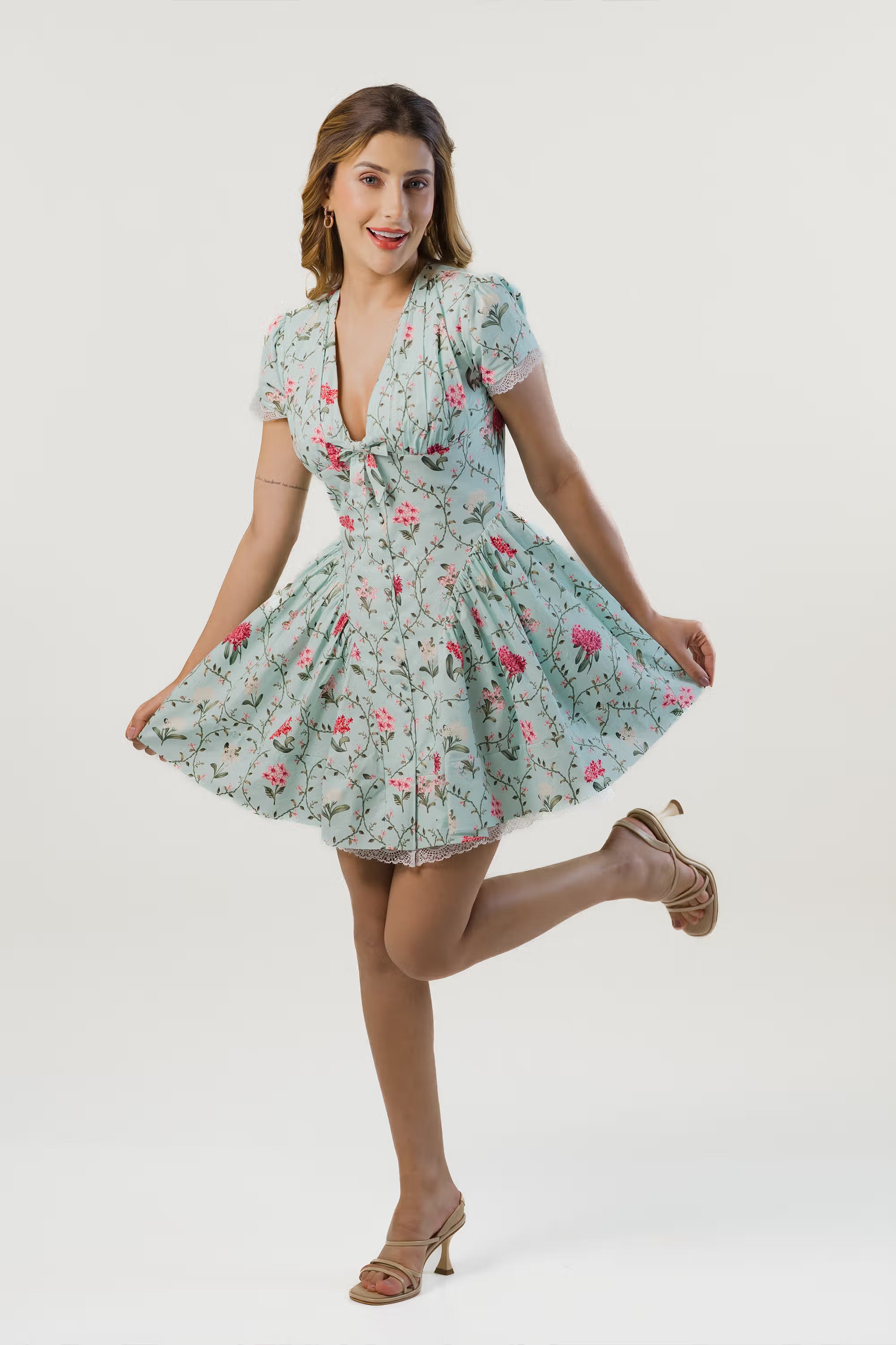 Woman in mint green floral mini dress with puff sleeves posing playfully and showing flared skirt