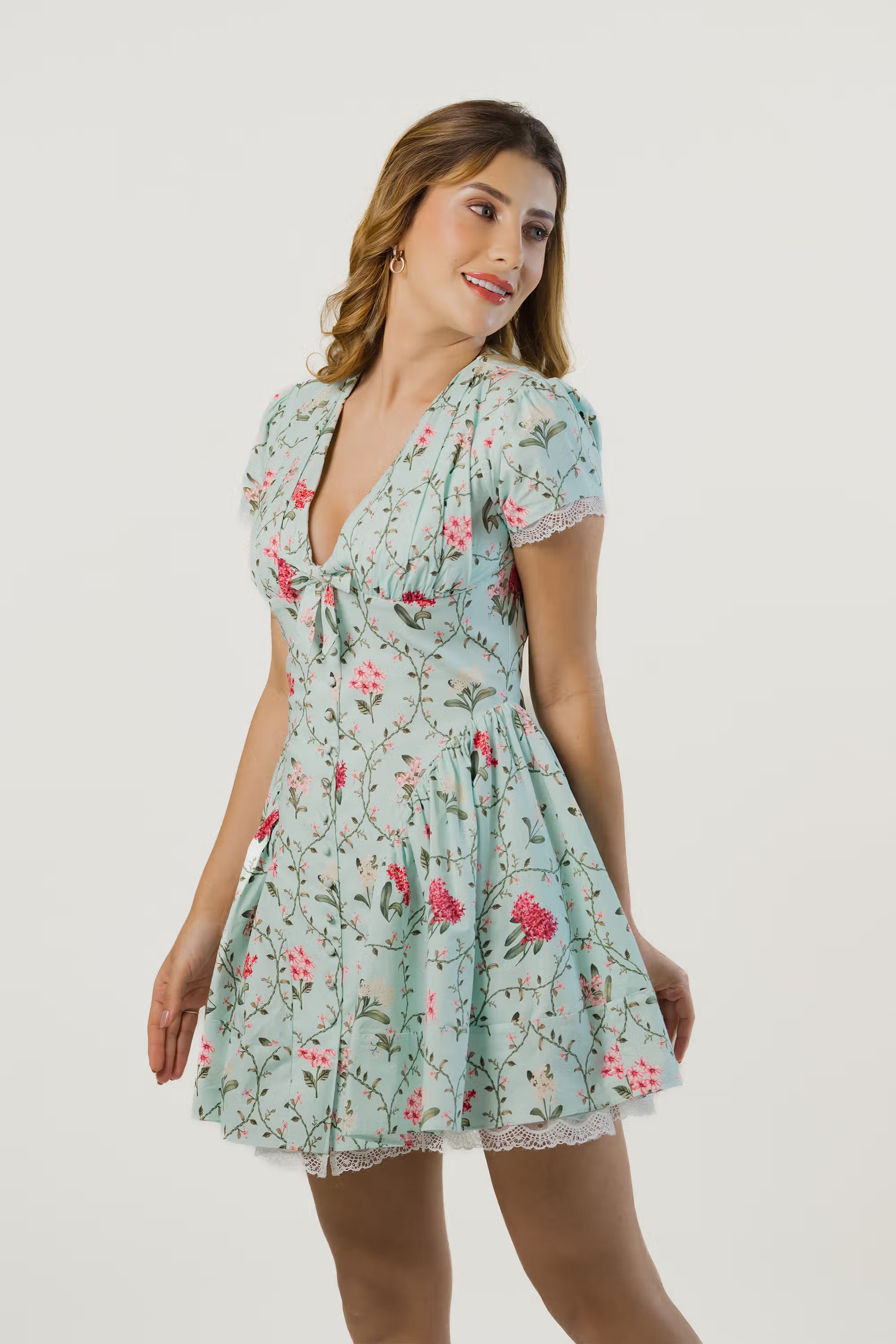 Woman smiling in mint green floral short dress with bow neckline and flared skirt