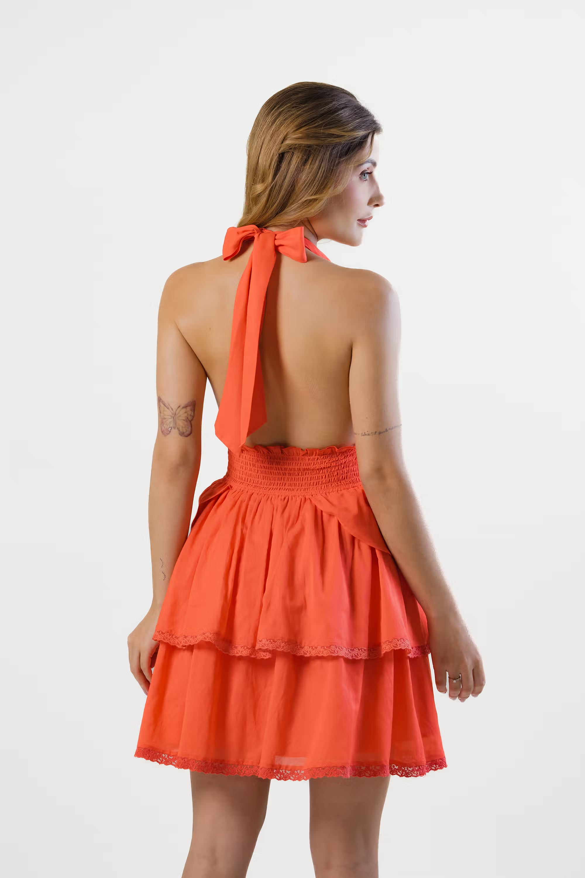 Back view of orange backless halter mini dress with tie-neck bow and tiered hemline
