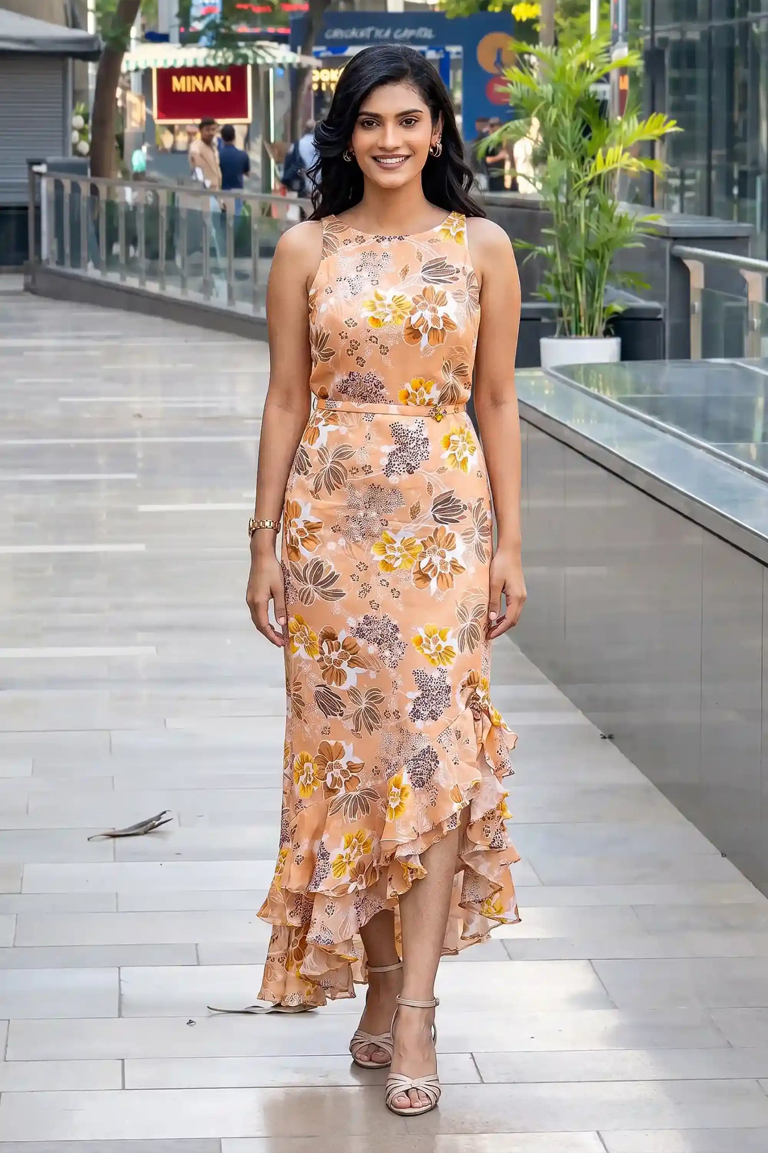 Woman in peach floral high-low maxi dress with sleeveless halter neckline and ruffle hem
