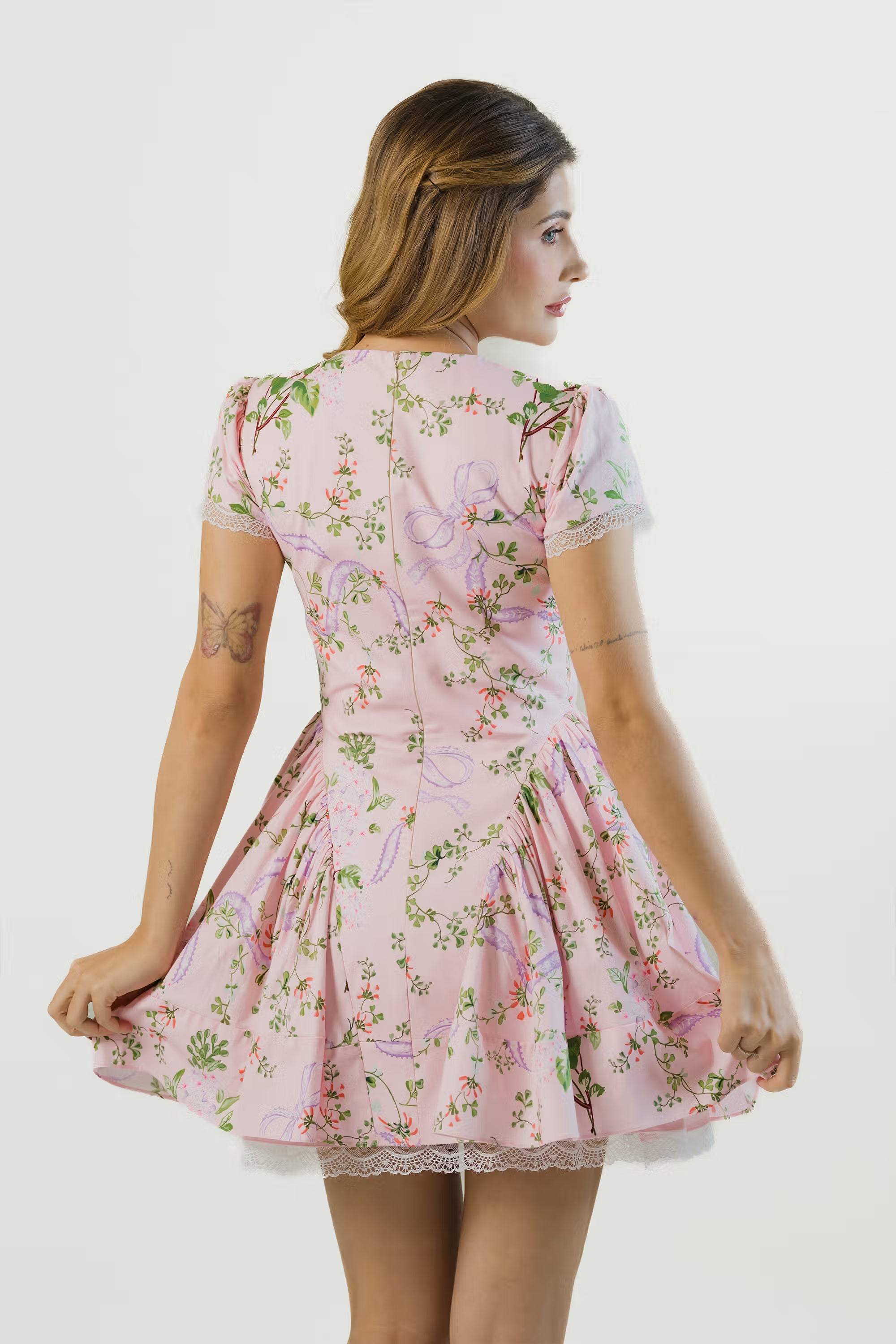 Back view of pink floral mini dress with short sleeves, bow prints, lace hem and flared silhouette.