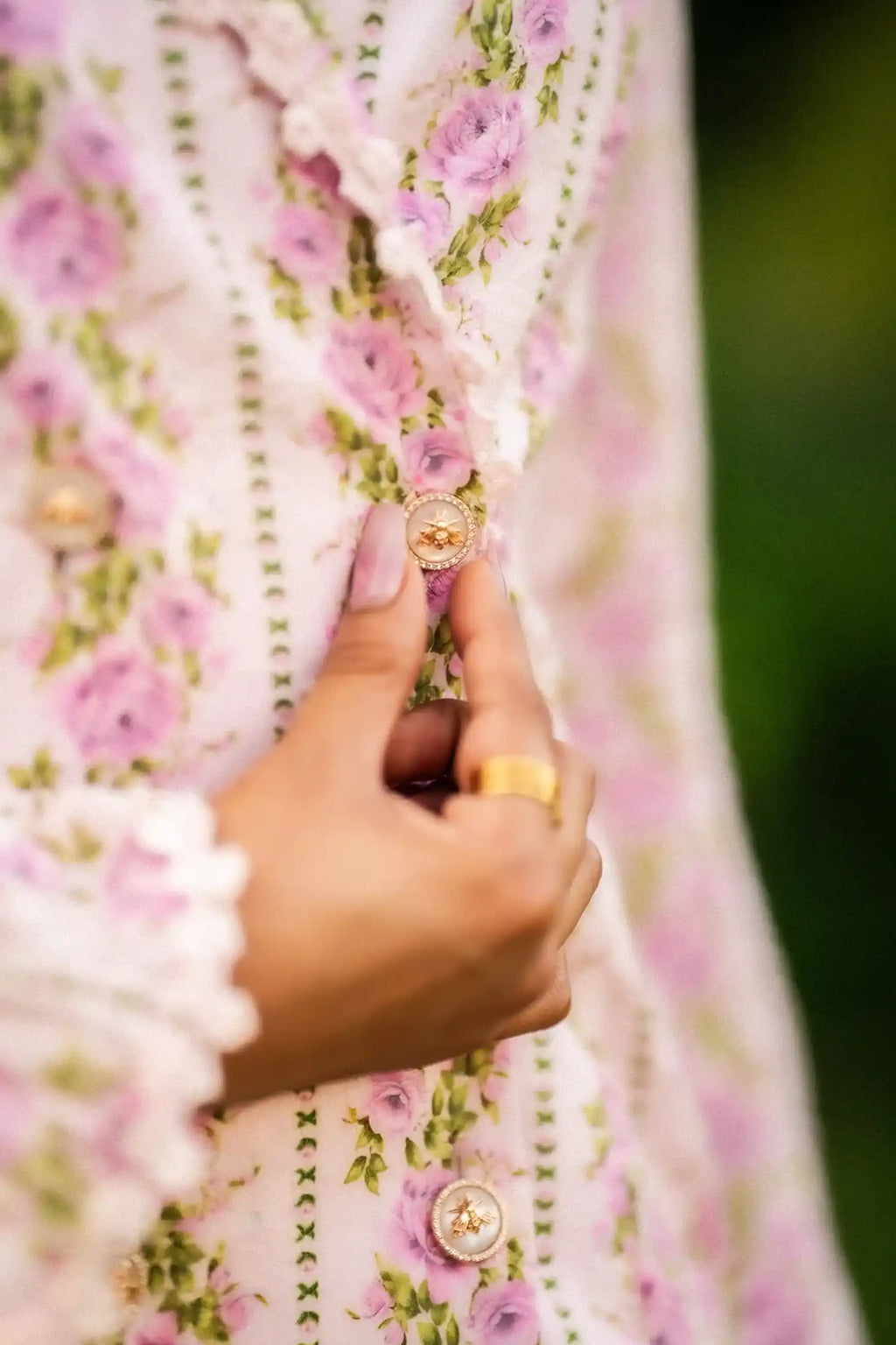Close-up detail of ornate gold bee buttons on pink floral dress