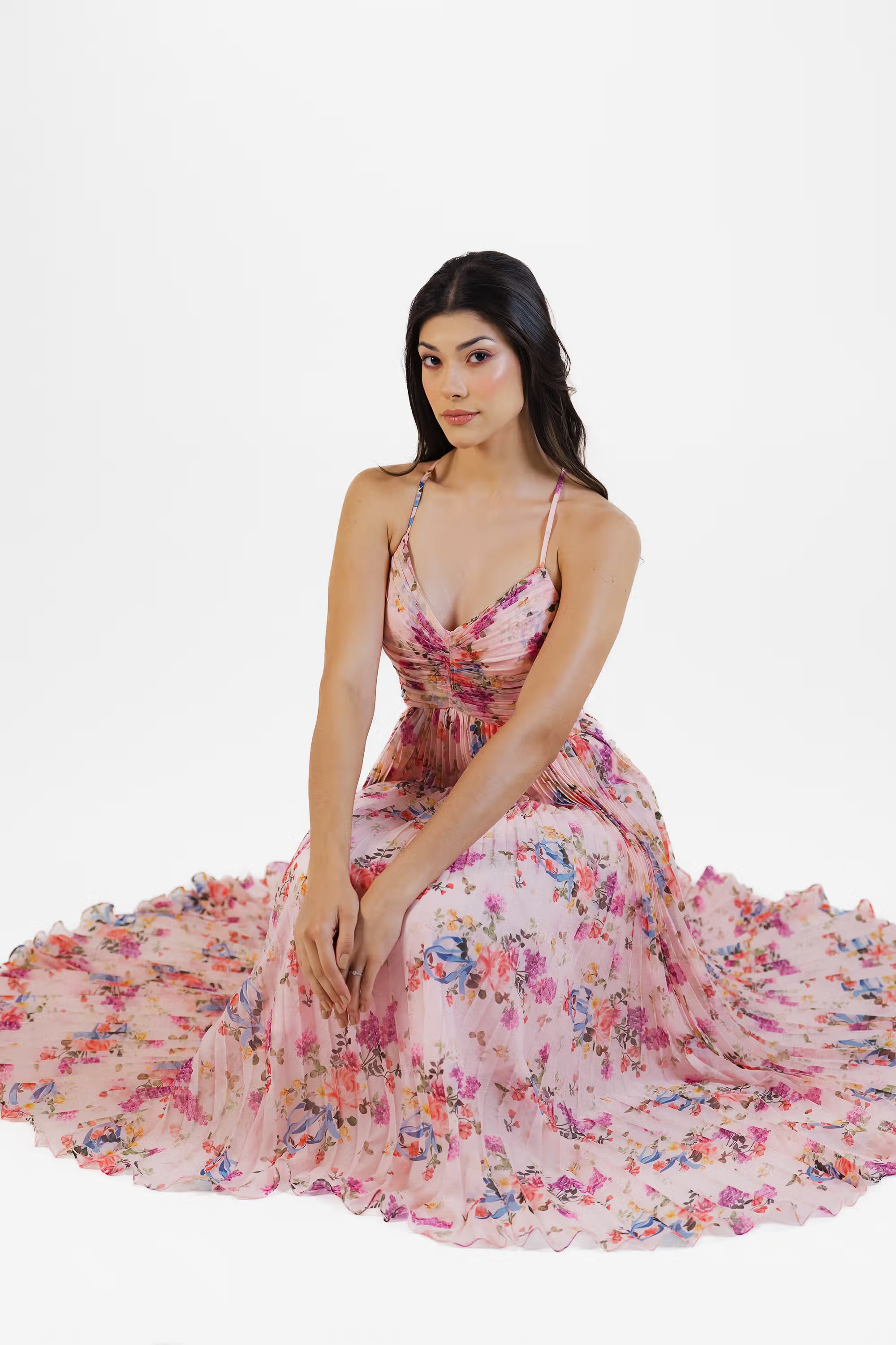 Women seated gracefully in pink floral pleated maxi dress with flowing skirt.