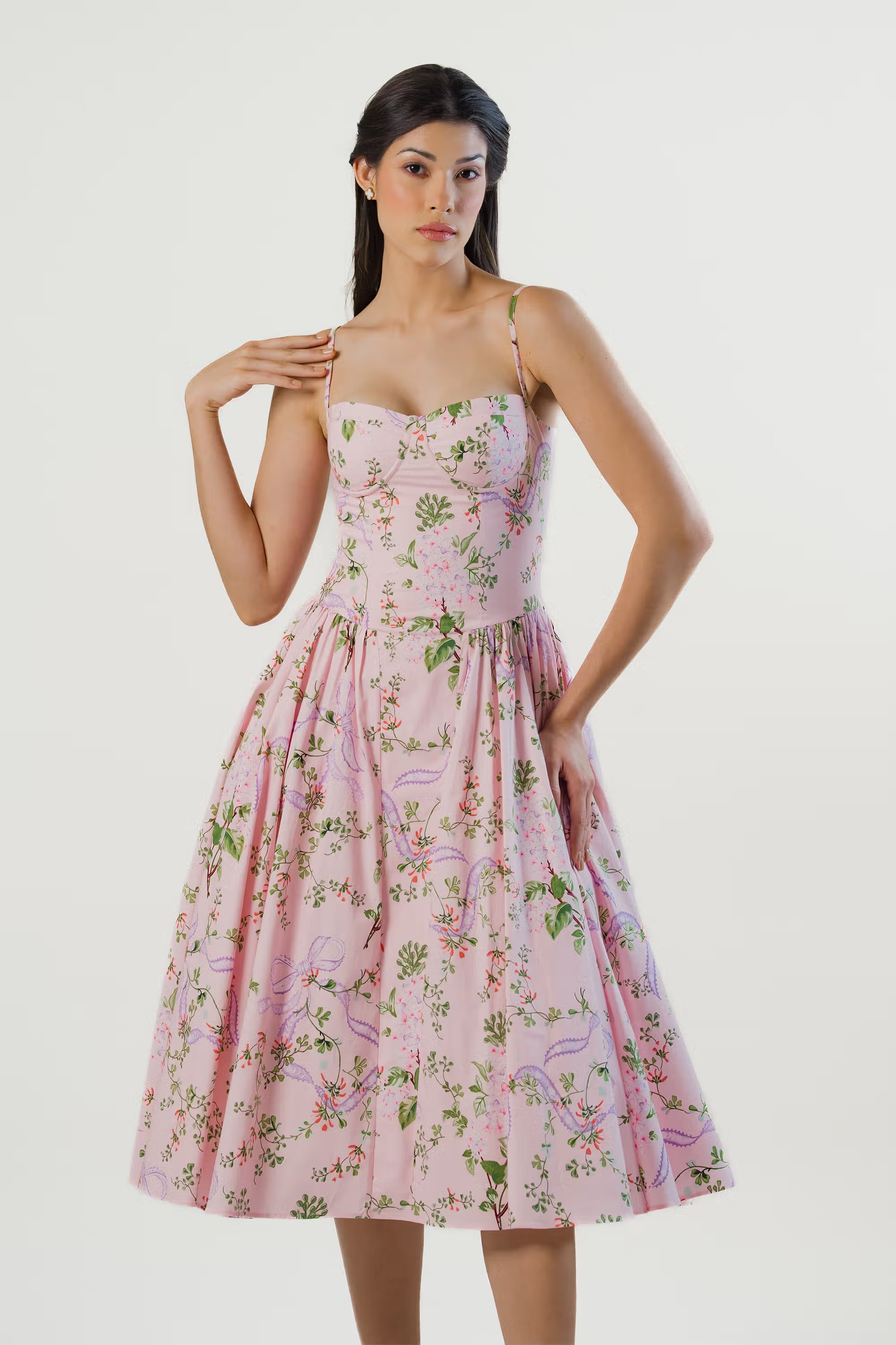 Elegant pink floral midi dress with bustier-style bodice, model posing with one hand lifted.