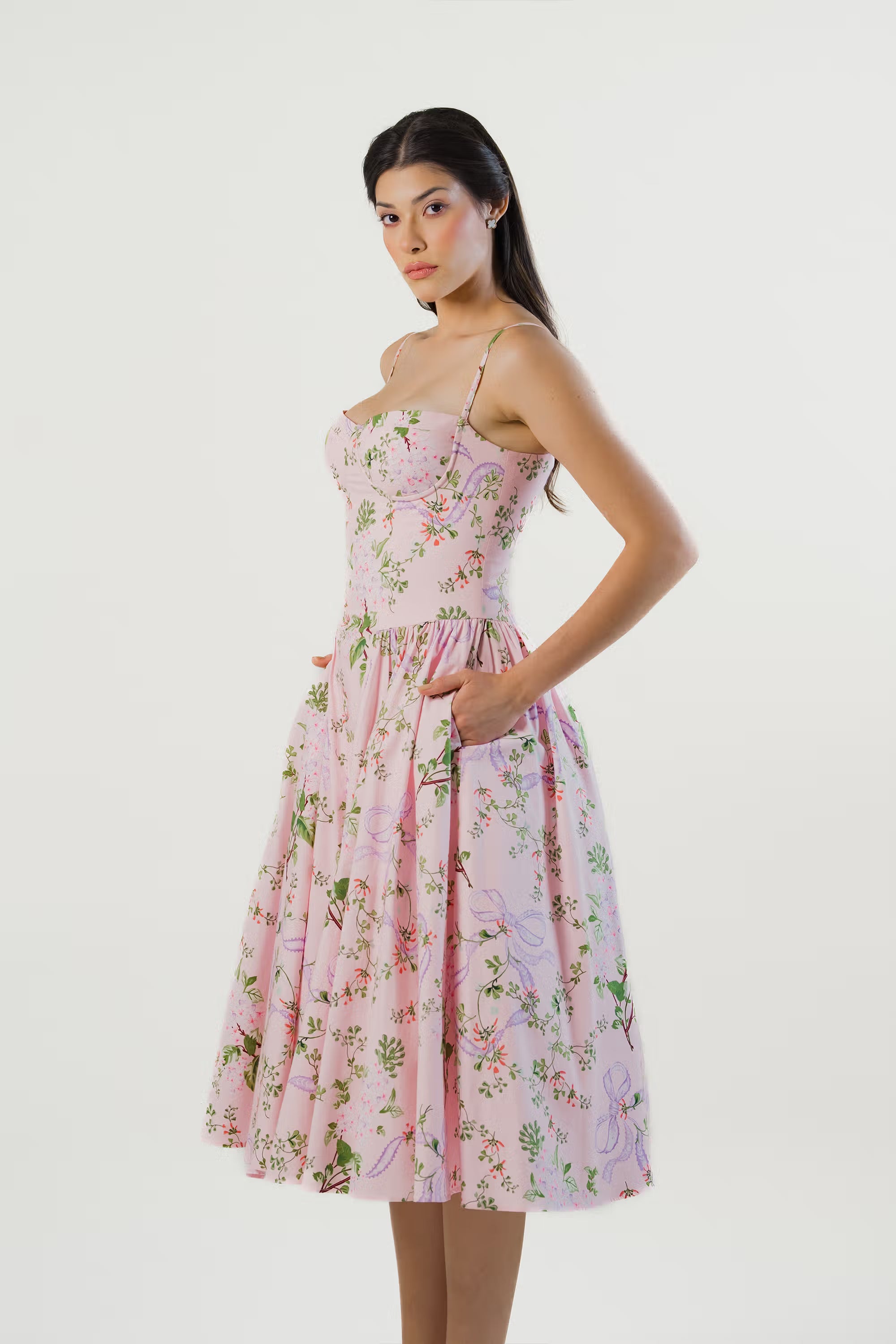 Women posing with hands in pockets, wearing a feminine pink floral sweetheart midi dress.