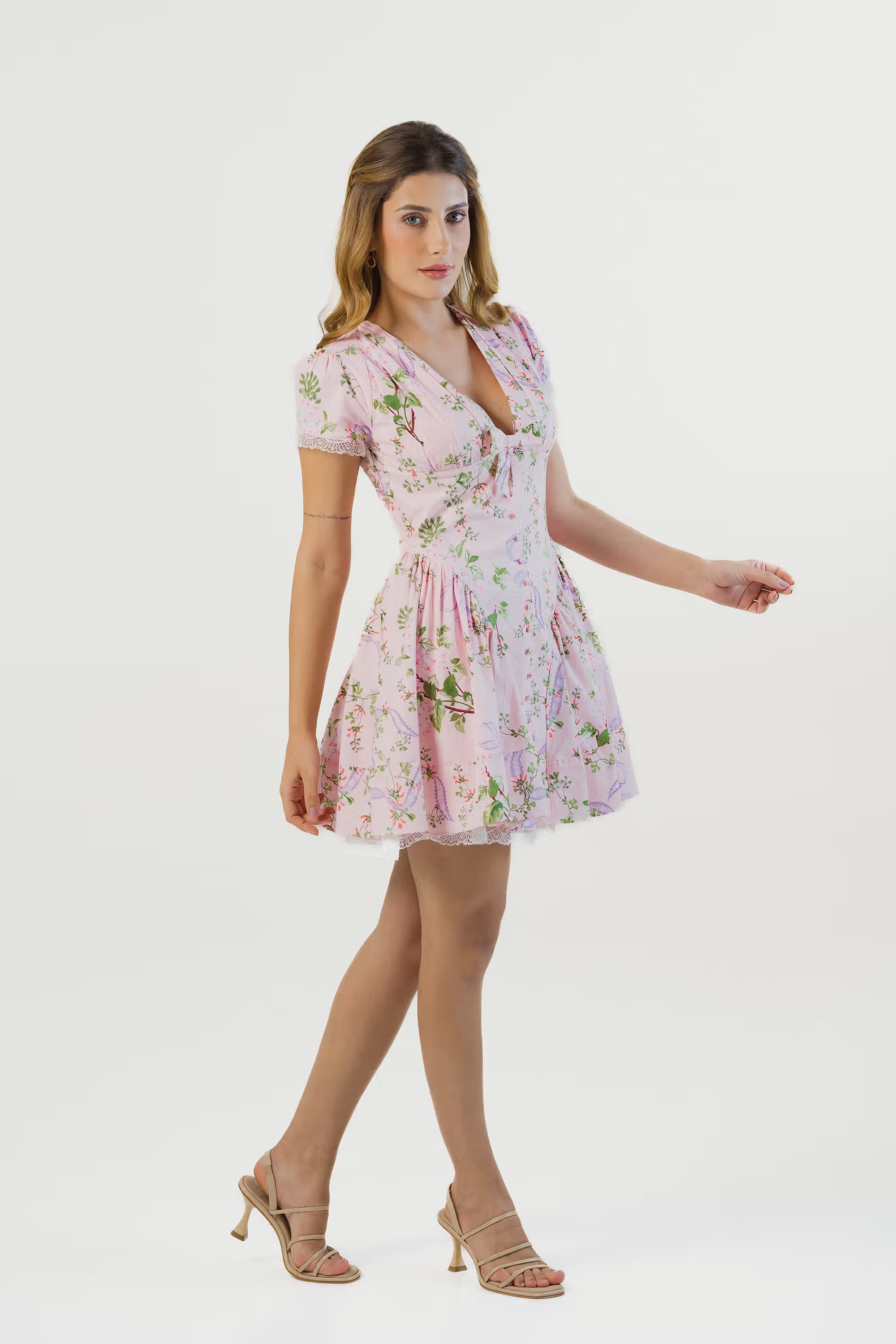 Side walking pose in pink floral mini dress with v-neck and short puff sleeves, lace trim hem.
