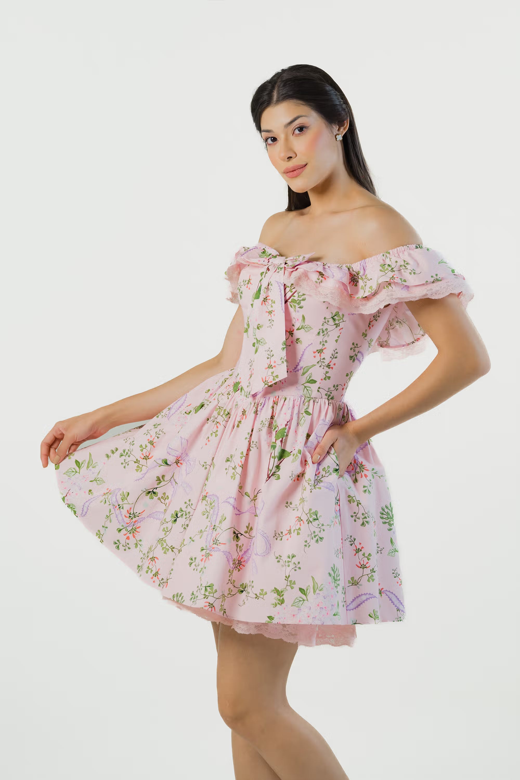 Woman posing sideways in pink floral off-shoulder mini dress with ruffle neckline and pockets