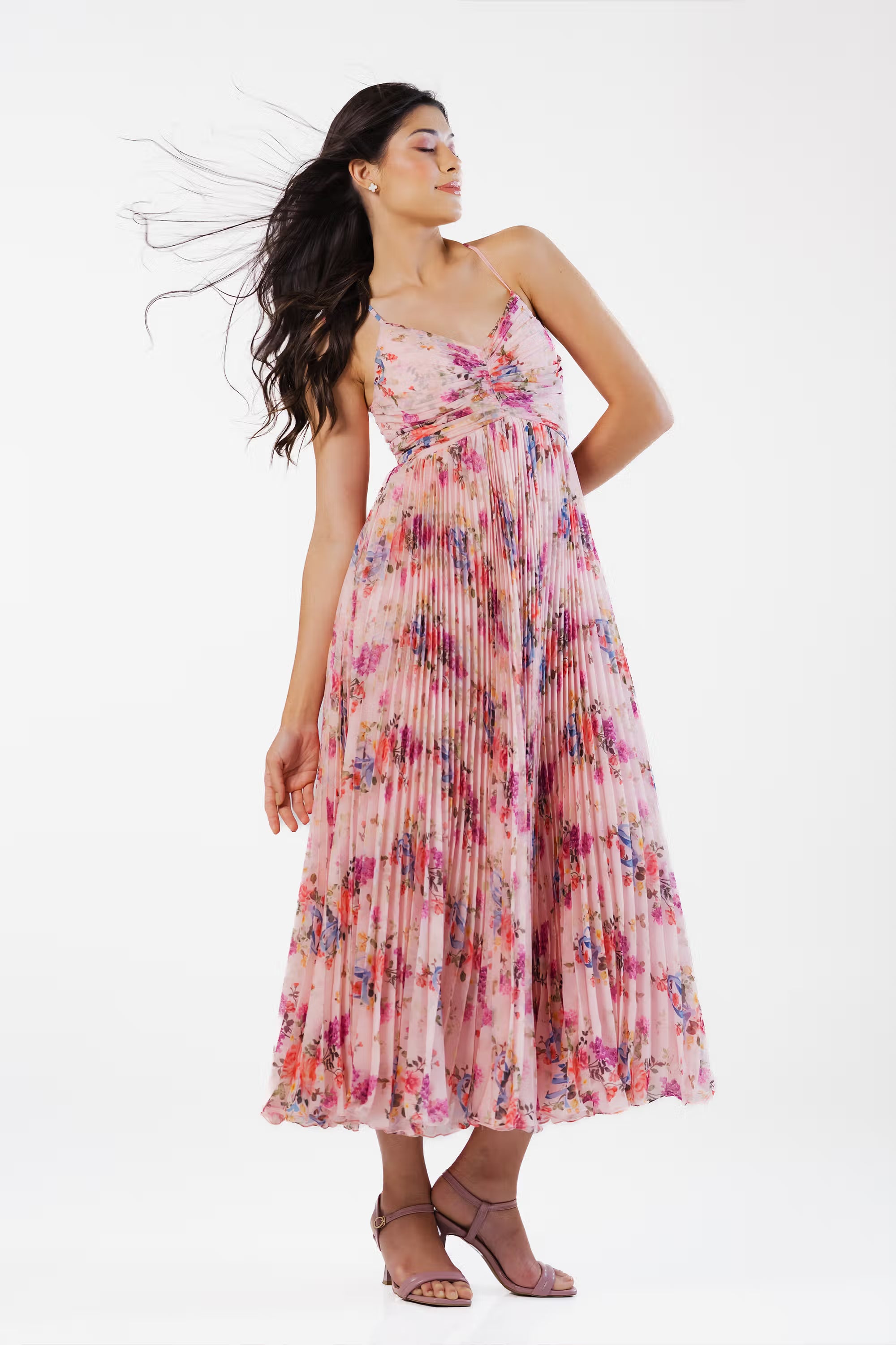 Women with hair flowing wearing pink floral pleated maxi dress with feminine silhouette.