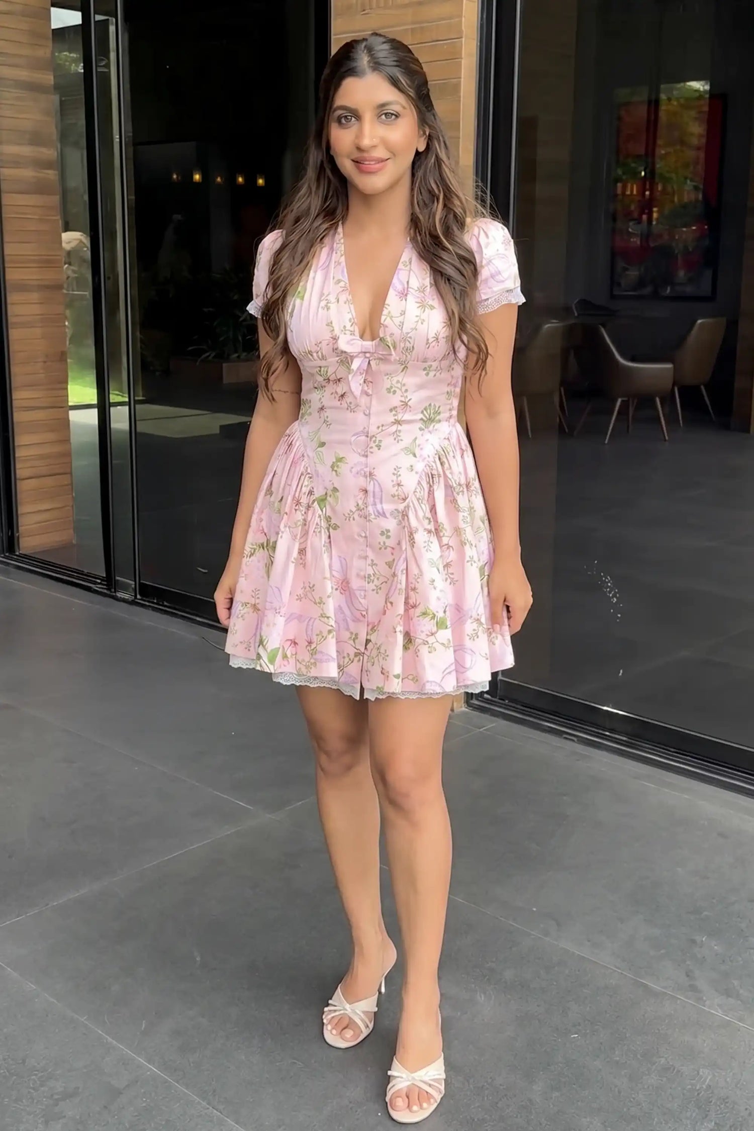 Woman in pink floral mini dress with V-neck tie bow, cap sleeves and lace-trim pleated skirt